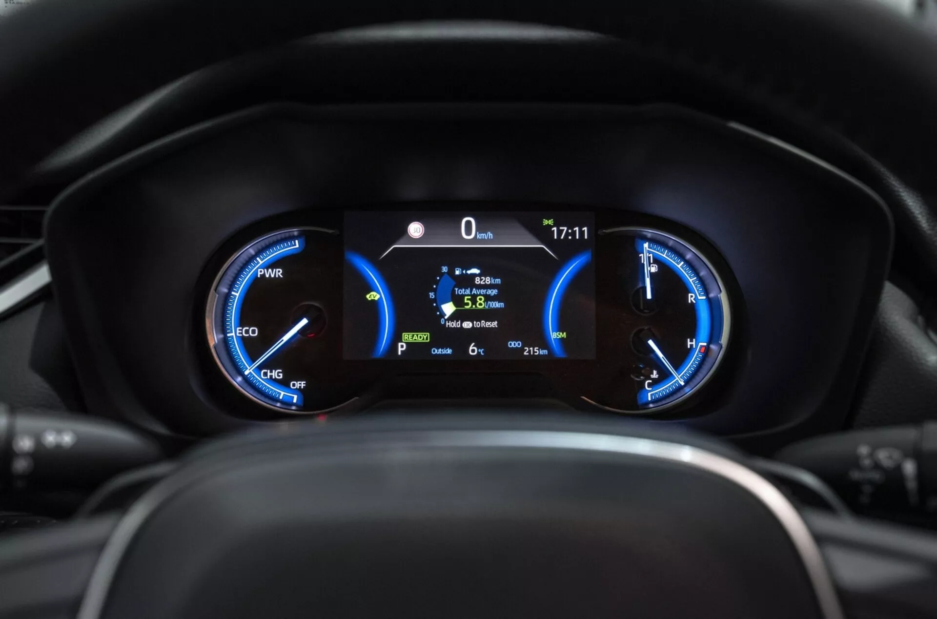 Närbild av Toyota RAV4 2019 instrumentkluster som visar hybridmätare med effektmätare, hastighetsmätare och central digital display som visar stillastående position, bränsleeffektivitet och utomhustemperatur ur förarens perspektiv.