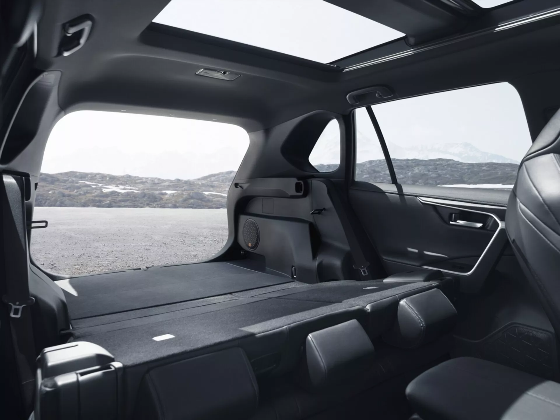 Interiörvy av en Toyota RAV4 2019 som visar det rymliga bakre kabinutrymmet från en hög vinkel, framhäver fällbara andra radens säten, omfattande lastutrymme, stora tonade fönster, modern design med premiummaterial, panoramasoltak, avancerat belysningssystem och klimatkontrollfunktioner
