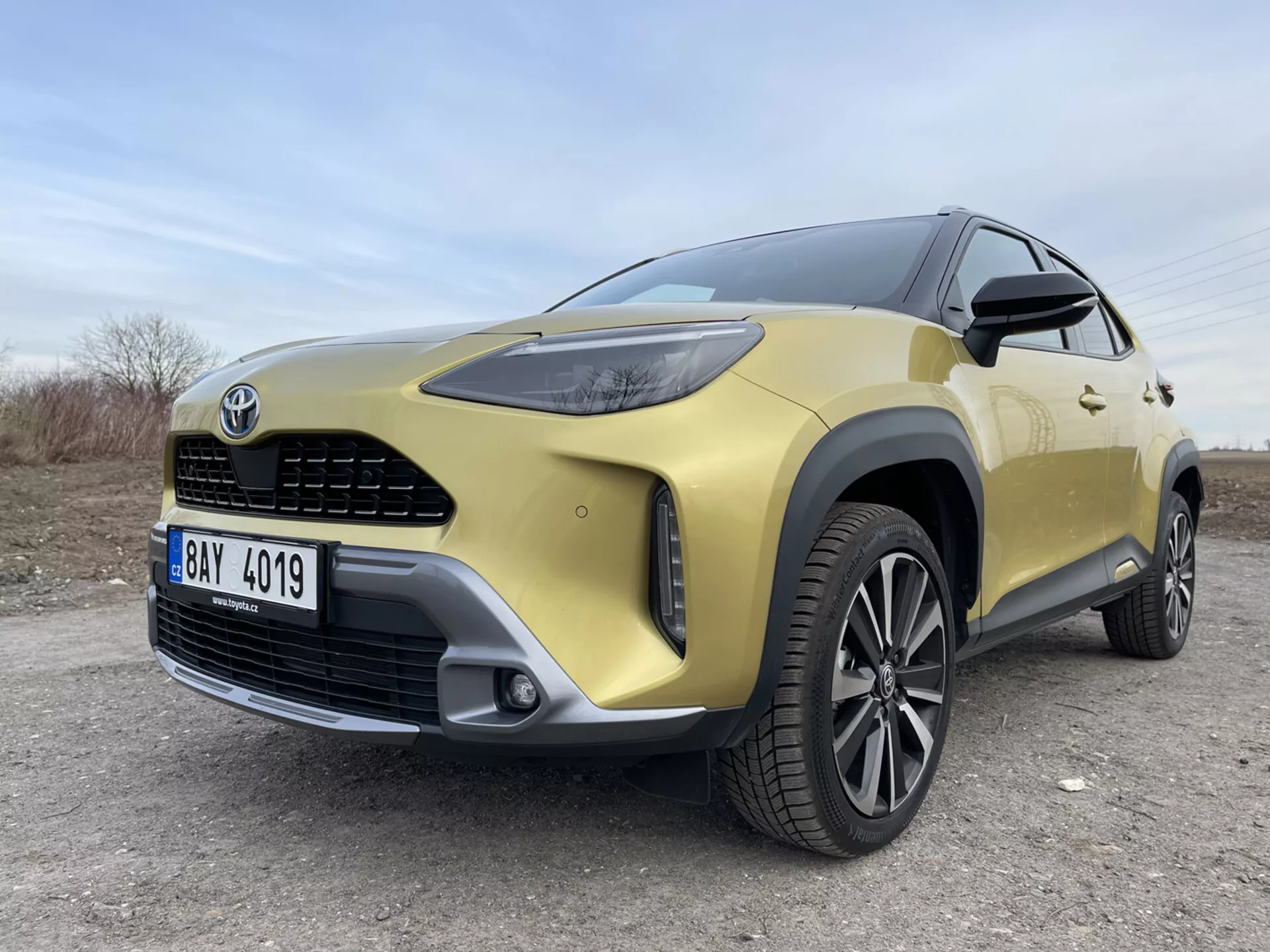 SUV Toyota Yaris-Cross 2021 i guld som visar dess främre vänstra kvartal från ett lågt vidvinkelperspektiv som lyfter fram LED-strålkastare, frontgrill, stötfångare, legeringsfälg och moderna designdetaljer på en oasfalterad yta