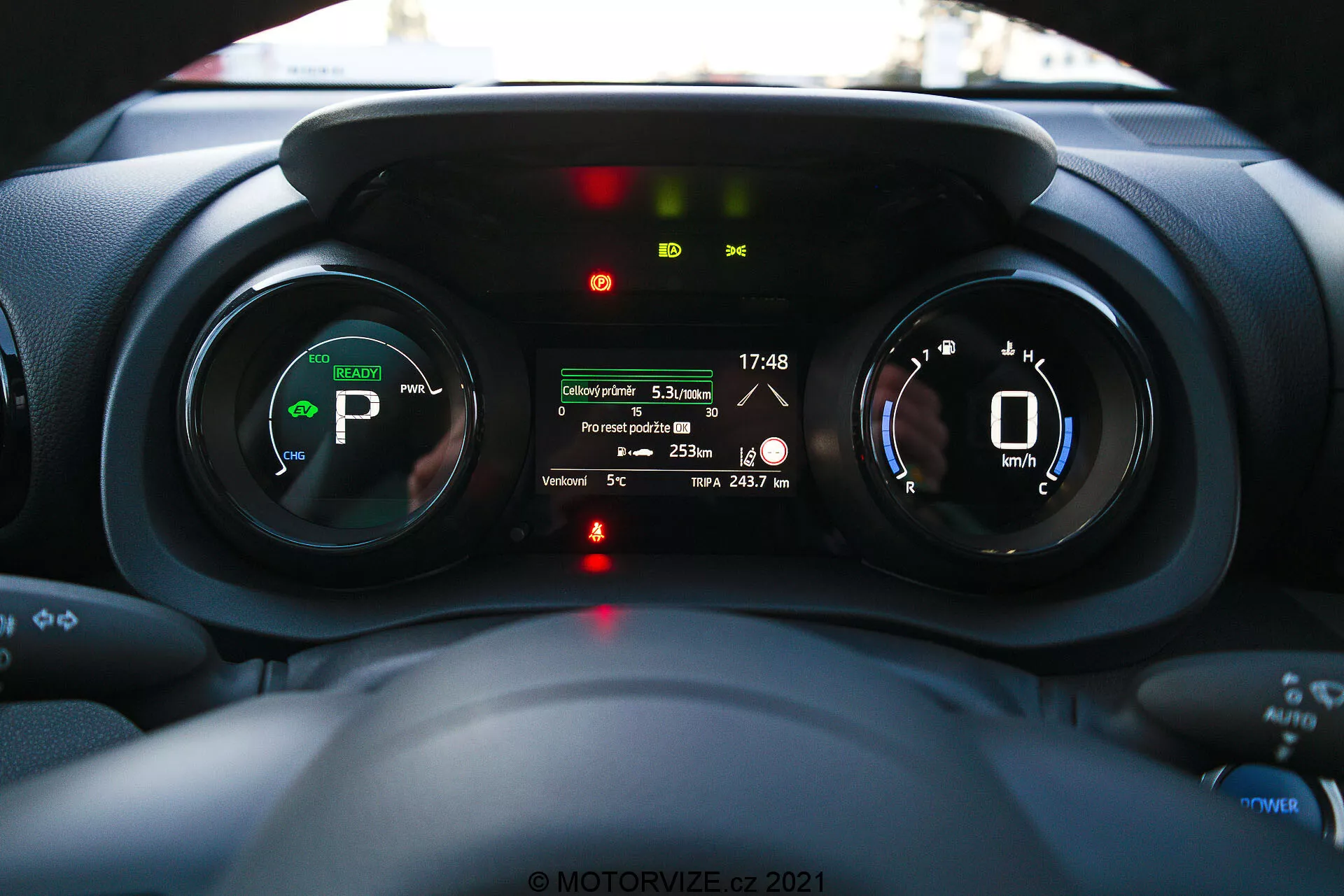 Interiörvy av Toyota Yaris 2020 instrumentbräda med fokus på instrumentpanelen, taget från förarens perspektiv som visar digitala mätare, indikatorer för elektriska eller hybrida fordon och en månginformationsdisplay med funktioner som körsträcka, utomhustemperatur och batteriräckvidd.