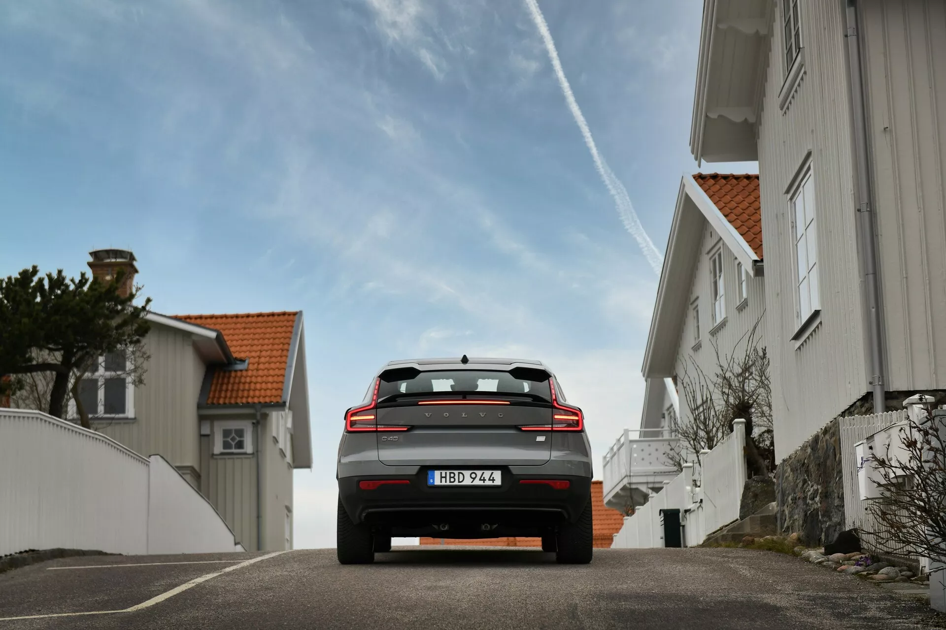 Volvo EC40 1:a generationen 2024 visas från ett bakifrån perspektiv, med höjd höjd, LED-bakljus, takspoiler och dubbla avgasrör på en europeisk gata som förmedlar dess hållning och väg närvaro med avancerade säkerhetsteknologier och en inblick i moderna designtrender inom bilindustrin