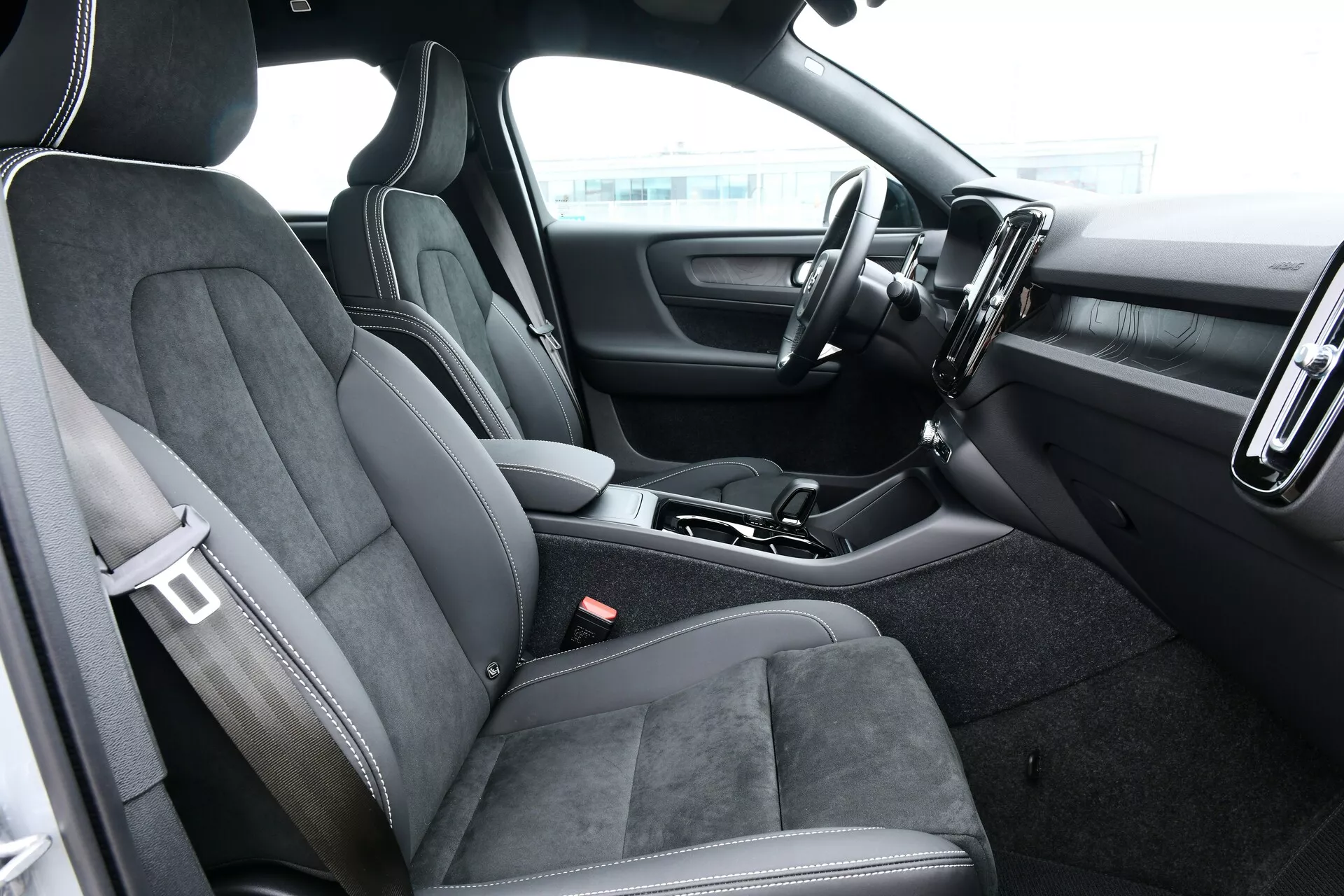 Interiörvy av Volvo EC40 2024 från förarsidan som visar ratten, instrumentbrädan, och mittkonsolen med sportiga och bekväma säten liknande Alcantara