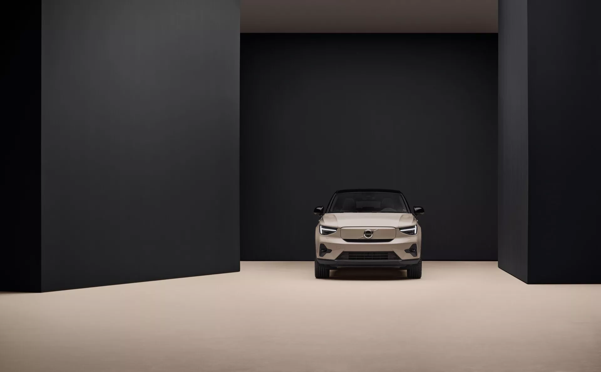 Volvo EC40 2024 1:a generationen placerad i en minimalistisk studioinställning med dämpad färgpalett, inramad av en stor rektangulär öppning, framhävande fordonets framsida inklusive LED-strålkastare, sluten grill och aerodynamisk design, som visar avancerad elektrisk fordons teknik och premium estetik.