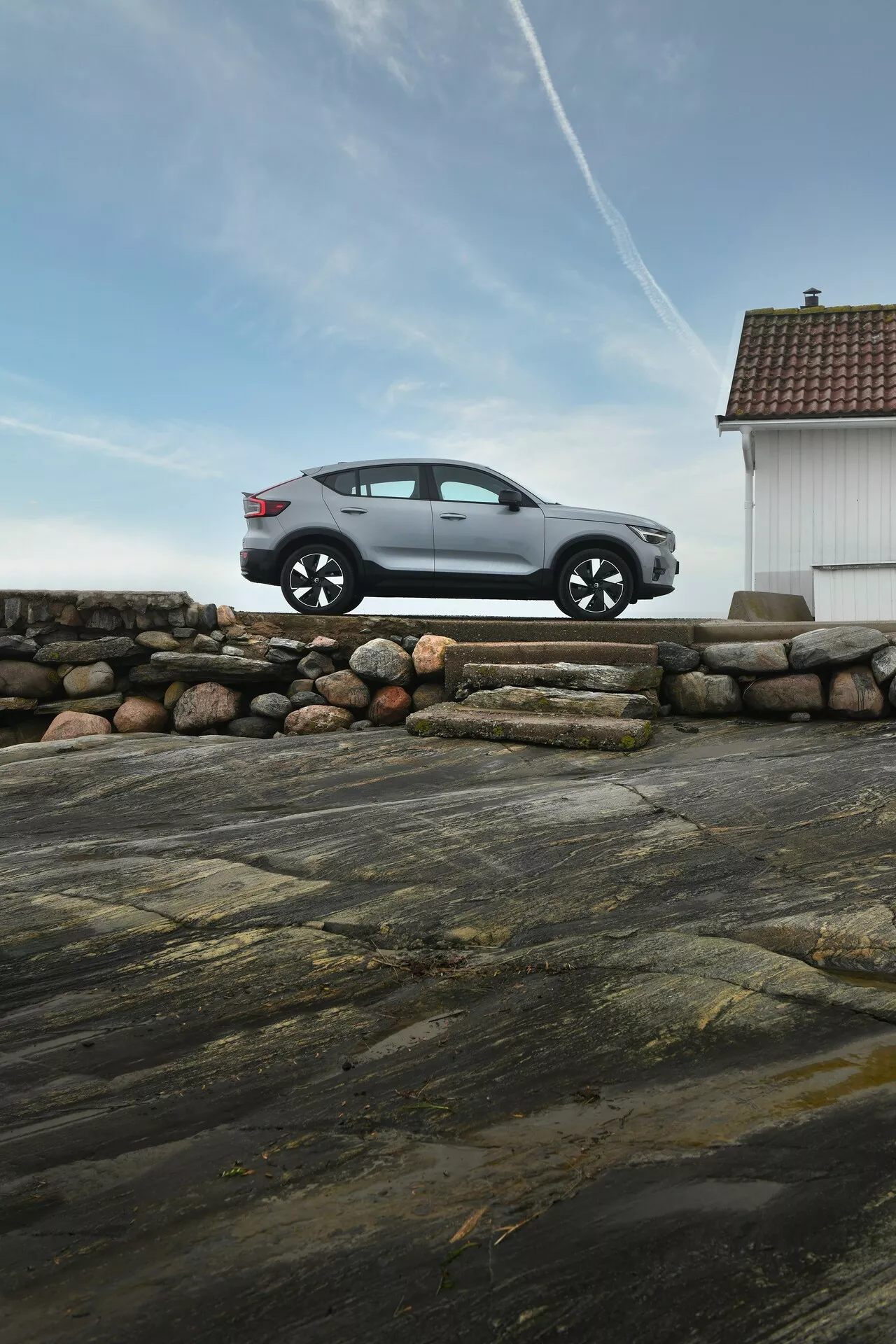 Volvo EC40 1:a generationen, fyradörrars hatchback i metallicfärg sedd från vänster sida på en kustnära stenmur, framhävande legerade hjul, snygg design och naturlig omgivning