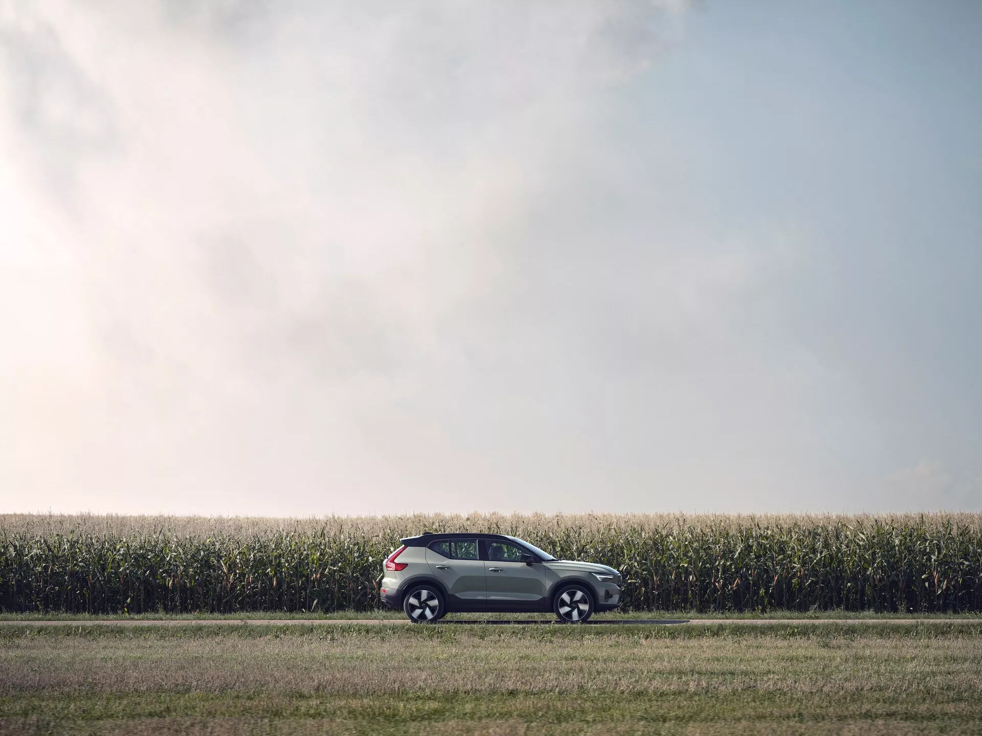 2024 Volvo EX40 av första generationen parkerad på grusväg bredvid majsfält som visar sidoprofil och tvåtonsfärgschema i mjukt ljus