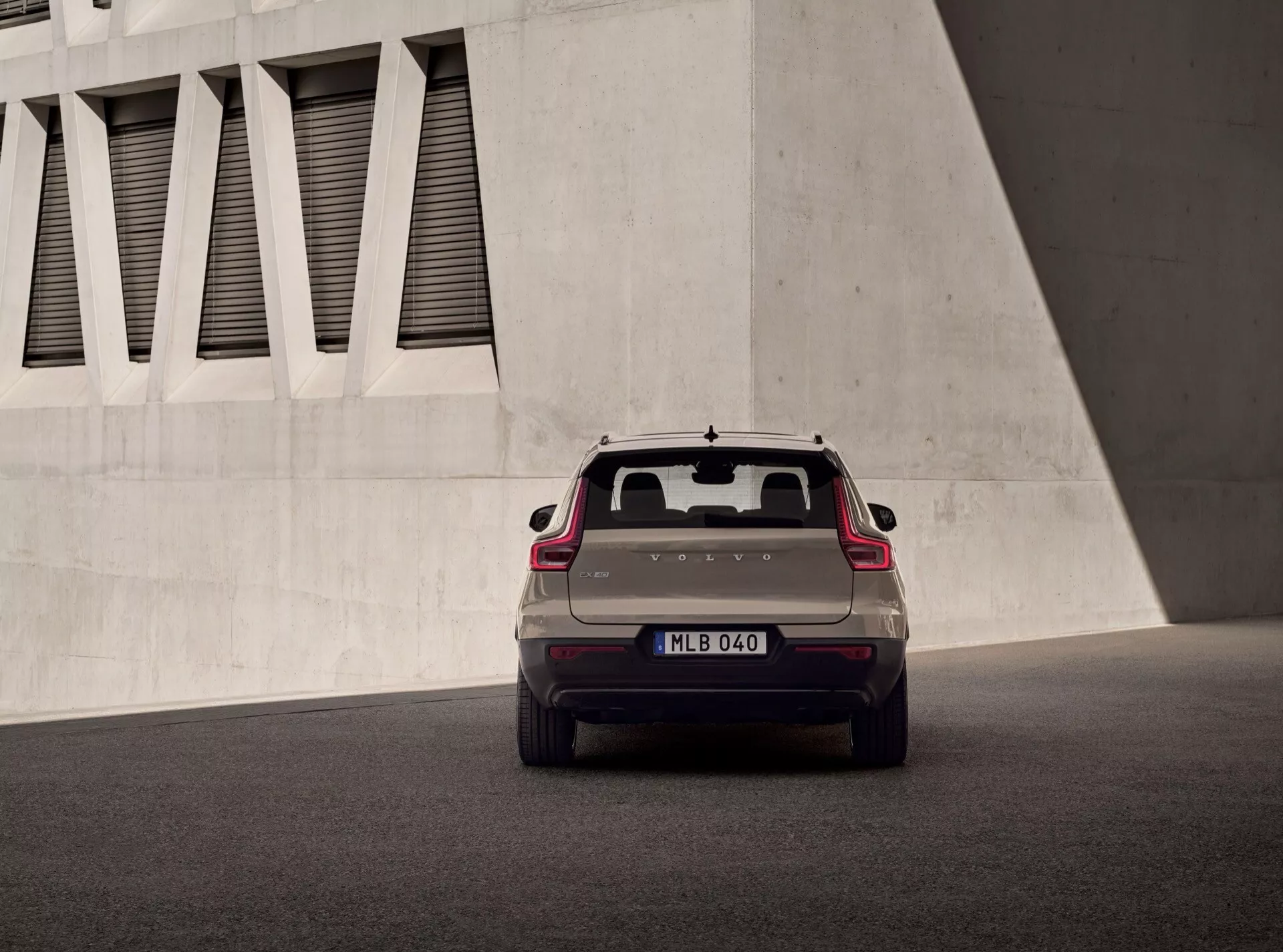 Volvo EX40 1:a generationen 2024 fångad bakifrån i låg vinkel som visar LED-baklampor, bakruta med avfrostare, dubbla avgassystem, europeiskt registreringsskylt, integrerad bagagelucka spoiler och parkeringsassistans teknik mot en modern arkitektonisk bakgrund