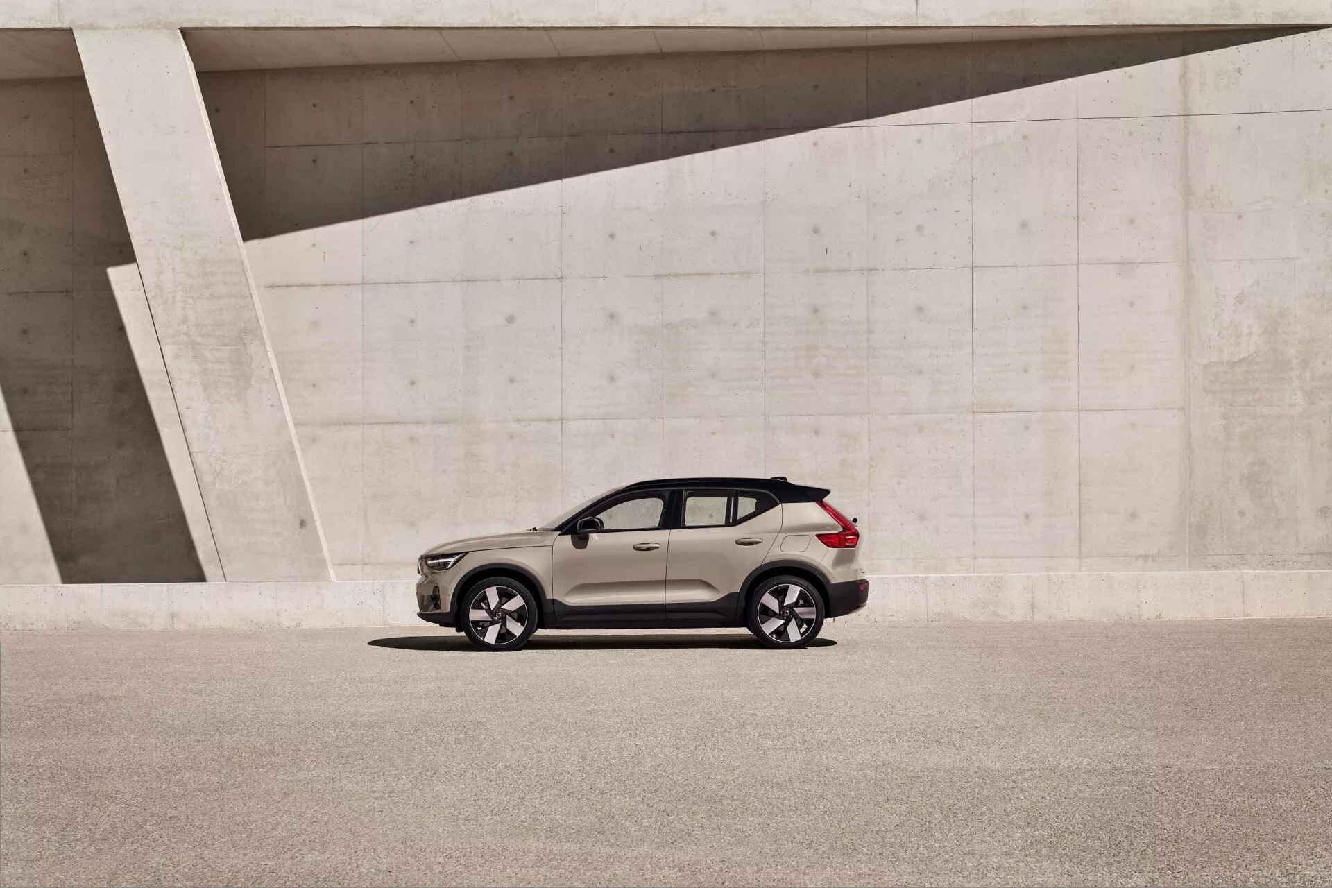 Volvo EX40 2024 1:a generationen, modern crossover SUV parkerad bredvid en vinklad betongstruktur, visar hela sidovy med naturligt ljus och detaljerade designdetaljer som legeringshjul och sluttande taklinje.