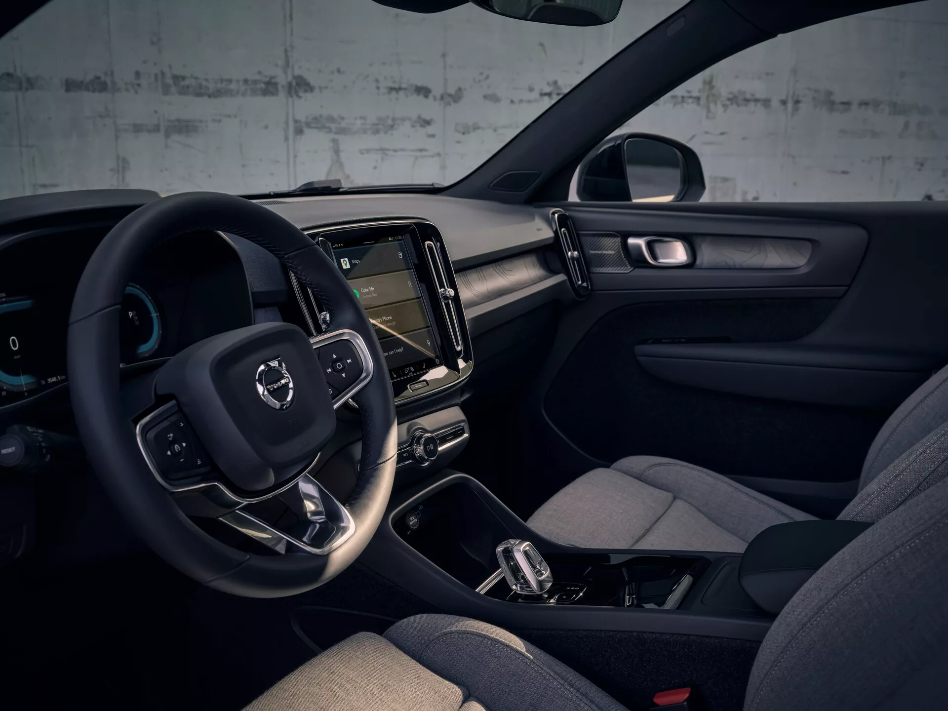 Interiörvy av Volvo EX40 första generationen 2024 med vänsterstyrning, digital instrumentpanel, vertikal pekskärmsinfotainment, minimalistisk instrumentbrädedesign, bekväma säten med sidostöd, automatisk växellåda med manuellt skiftläge, integrerad omgivningsbelysning, färgschema i mörka toner och avancerade teknikelement.