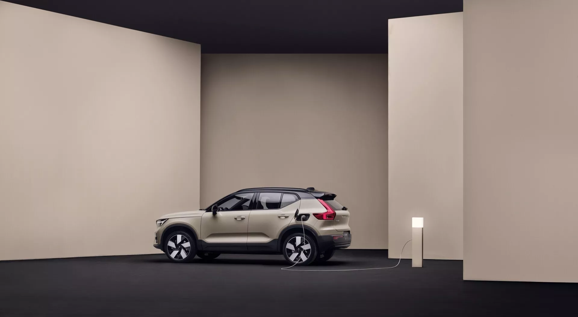 Volvo EX40 första generationen 2024 i studiomiljö som visar sin stilrena design, vit eller silverfärg, ansluten till en laddningsstation som indikerar egenskaper hos elbilen, positionerad för att visa bilens profil och framsida