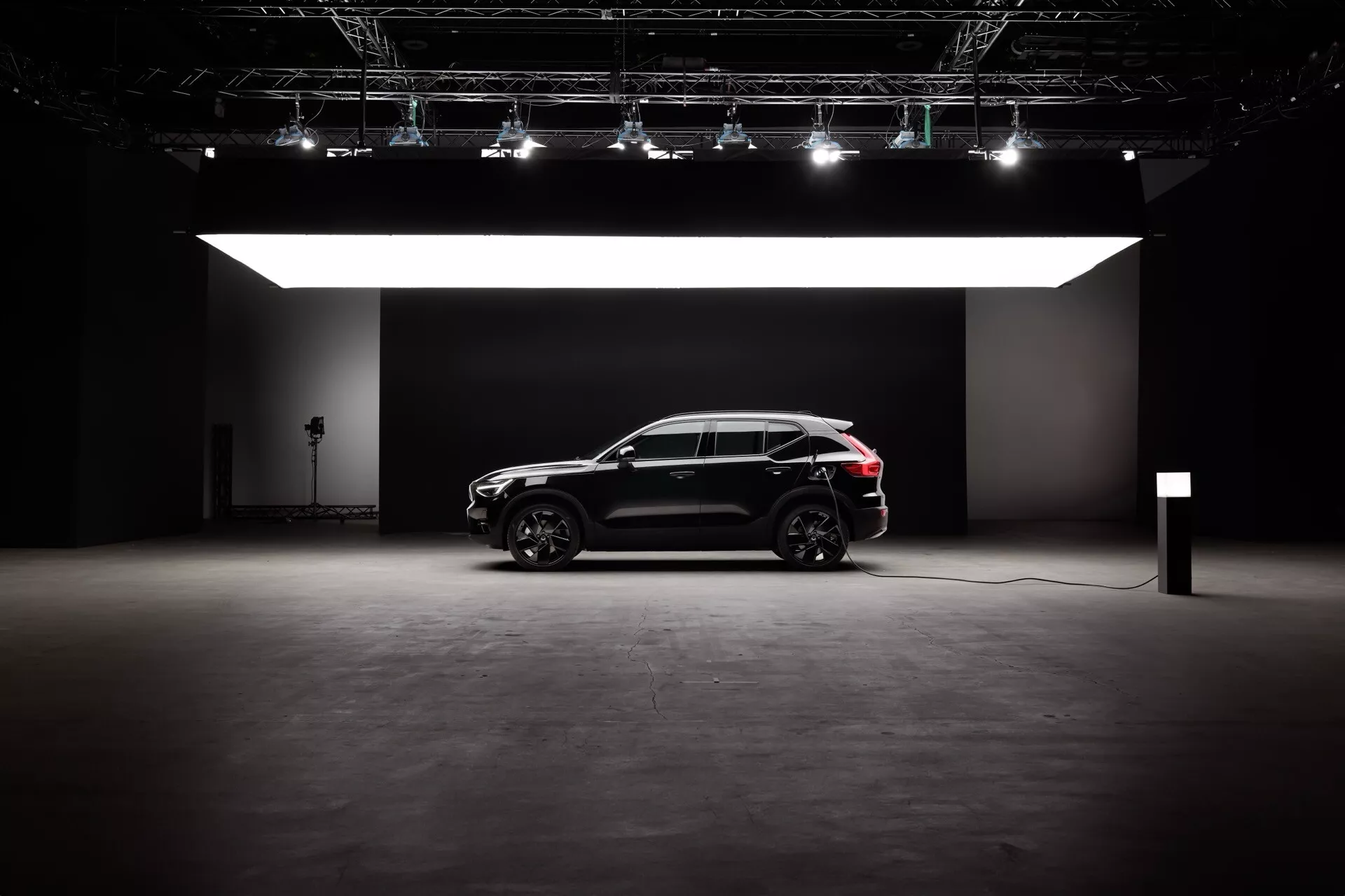 Sidoprofil av Volvo EX40 1:a generationen 2024 i en studioinställning, som visar dess eleganta svarta exteriör, modern SUV-design med en sportig crossover-stil, och elektriska/hybrida möjligheter. Funktioner inkluderar stora hjul med flerspakig legeringsdesign, dramatisk belysning utan reflektion och en laddningskabel som indikerar hållbar motor teknologi.