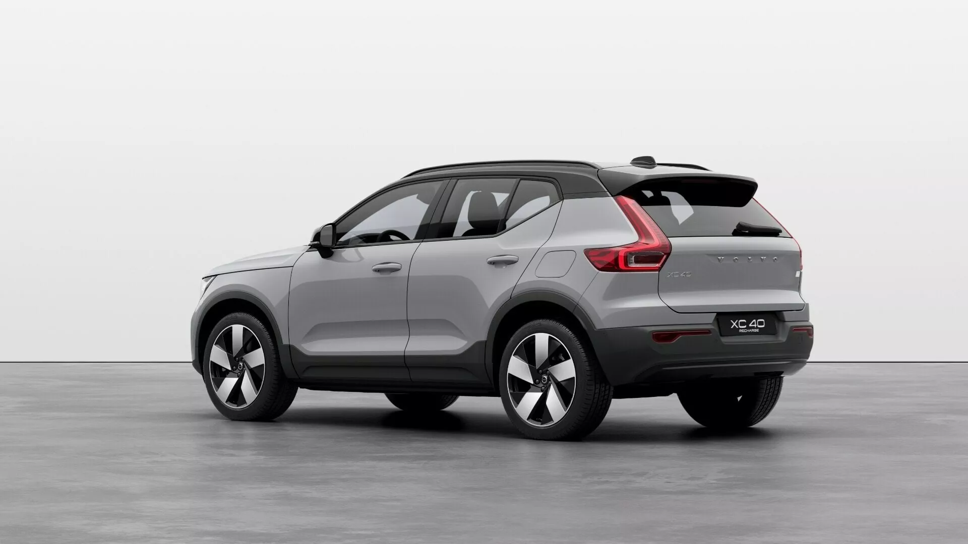 Volvo EX40 första generationen 2024 i en trekvarts bakvy som visar dess kompakt till mellanstor SUV-kaross, sportigt sluttande bakre taklinje, integrerad bakspoiler, LED-bakljus med modern ljussignatur, dubbla avgastips, flerspakiga legeringshjul och sidospeglar med integrerade blinkers i en studioinställning.