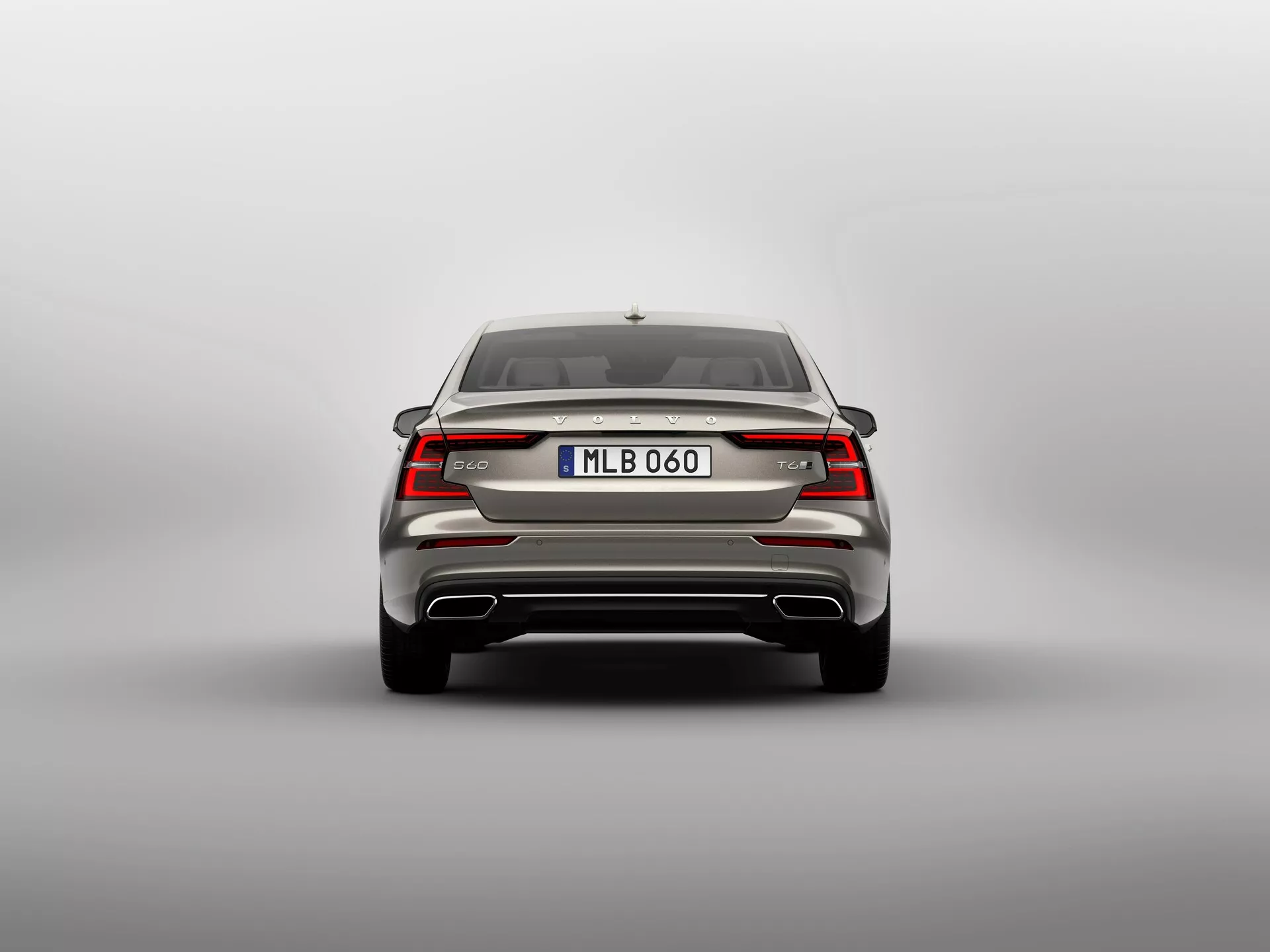 Bakre vy av en modern 2018 Volvo S60-V60 tredje generationens sedan, som visar en symmetrisk design med eleganta horisontella LED-bakljus som möts vid märkesemblemet, integrerad bagagespoiler, robust bakre stötfångare med reflexer och eventuellt parkeringssensorer, modellbeteckning, europeisk stil registreringsskylt med potentiell backkamera, dubbla avgasrör, hajfensantenn och bakruta med avfrostare, fångad i en rak vinkel i ögonhöjd mot en neutral bakgrund.