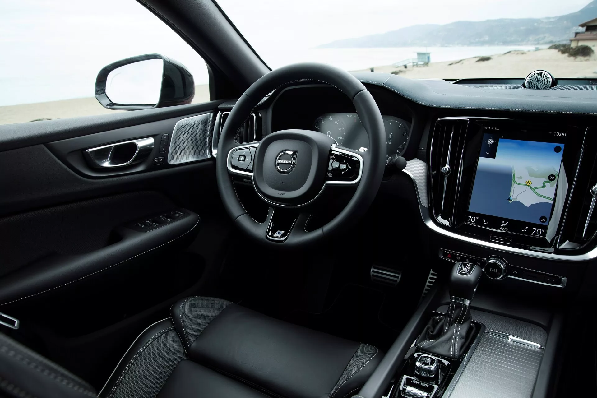 Interiörvy av en modern Volvo S60-V60 2018 (3:e generationen) från främre passagerarsätets perspektiv, med ett tre-ekrad ratt med inbyggda kontroller, digitala instrumentkluster, stor vertikal infotainment-pekskärm med navigeringskarta, minimalistiska HVAC-kontroller, elegant växelspak, mörk färgskala med metallinslag och avancerat ljudsystem.