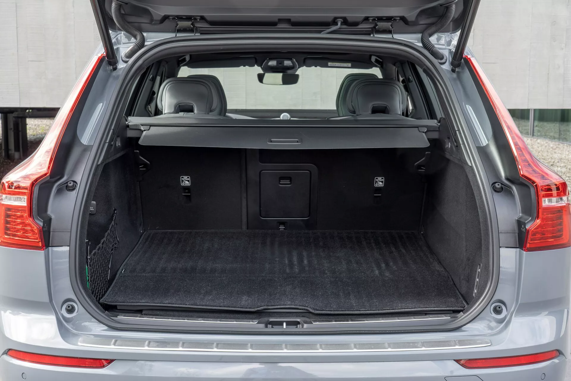 Bakre lastutrymme i en 2021 Volvo XC60 (andra generationens facelift), som visar det öppna bagageutrymmet från en rak bakifrån synvinkel med ett tomt lastutrymme, delvis utdragbart lastskydd, skyddsmatta, plastbeklädnad med små förvaringsutrymmen, eventuell 12-voltsuttag, metalltröskel och fällbara baksäten med nackstöd.
