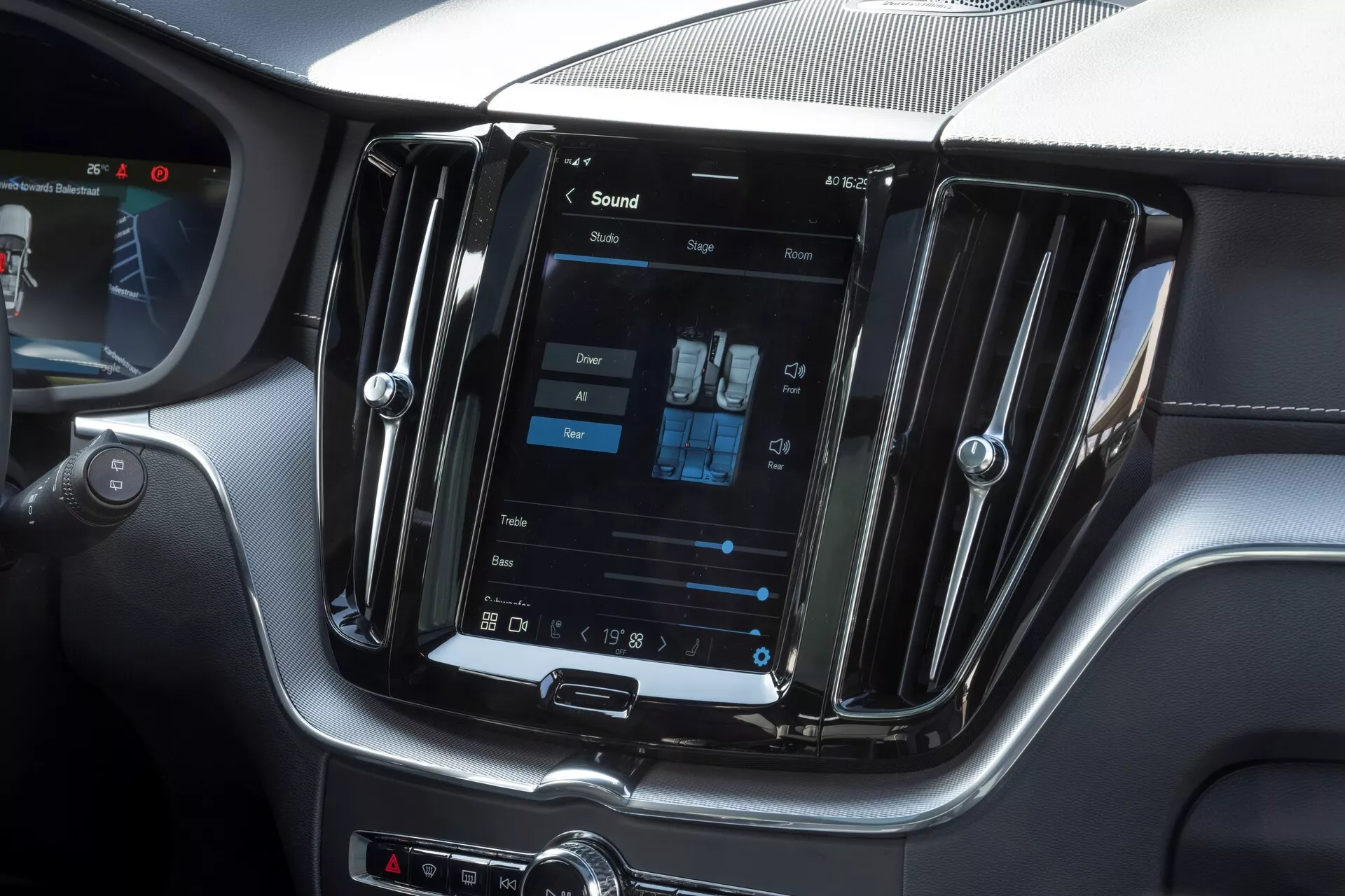Interiörbild av en Volvo XC60 2021 facelift som fokuserar på mittkonsolen med ett stort, vertikalt orienterat pekskärmsystem för infotainment. Bilden är tagen ur passagerarperspektiv och visar även inställningar för dubbel klimatkontroll, metalliska ventilationsgaller och manuella kontrollknappar under skärmen, vilket ger en modern och lyxig känsla.