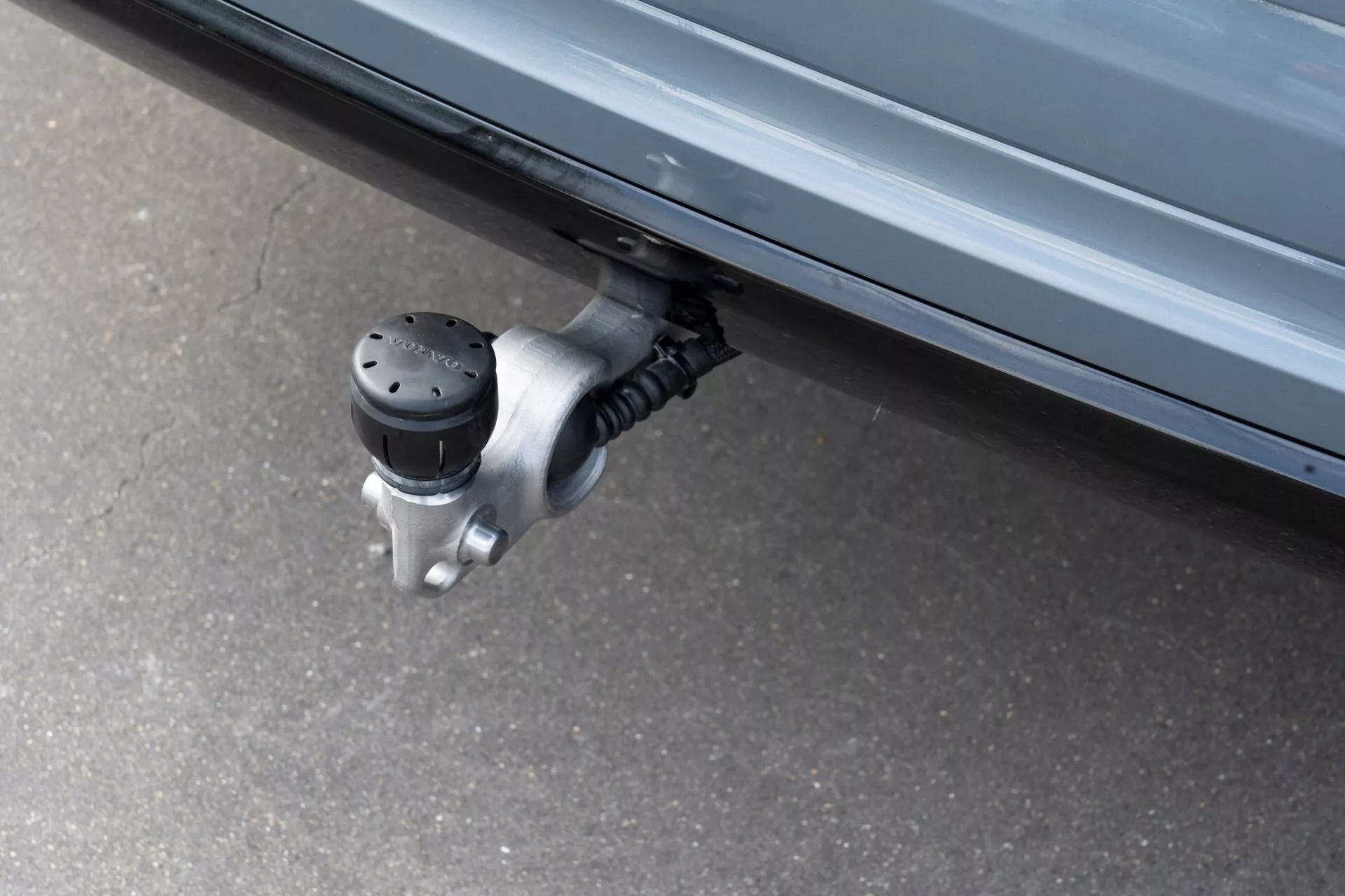 Närbild av ett infällbart sidosteg på en Volvo XC60 2021 (2:a generationen-facelift), som visar den utsträckta halkskyddade ytan med upphöjda svarta prickar under fordonets sidodörr, fäst vid en metallisk gångjärnsmekanism. Fotograferad från låg vinkel, framhäver den automatiska funktionen som är utformad för att underlätta in- och urstigning genom att minska avståndet till marken.