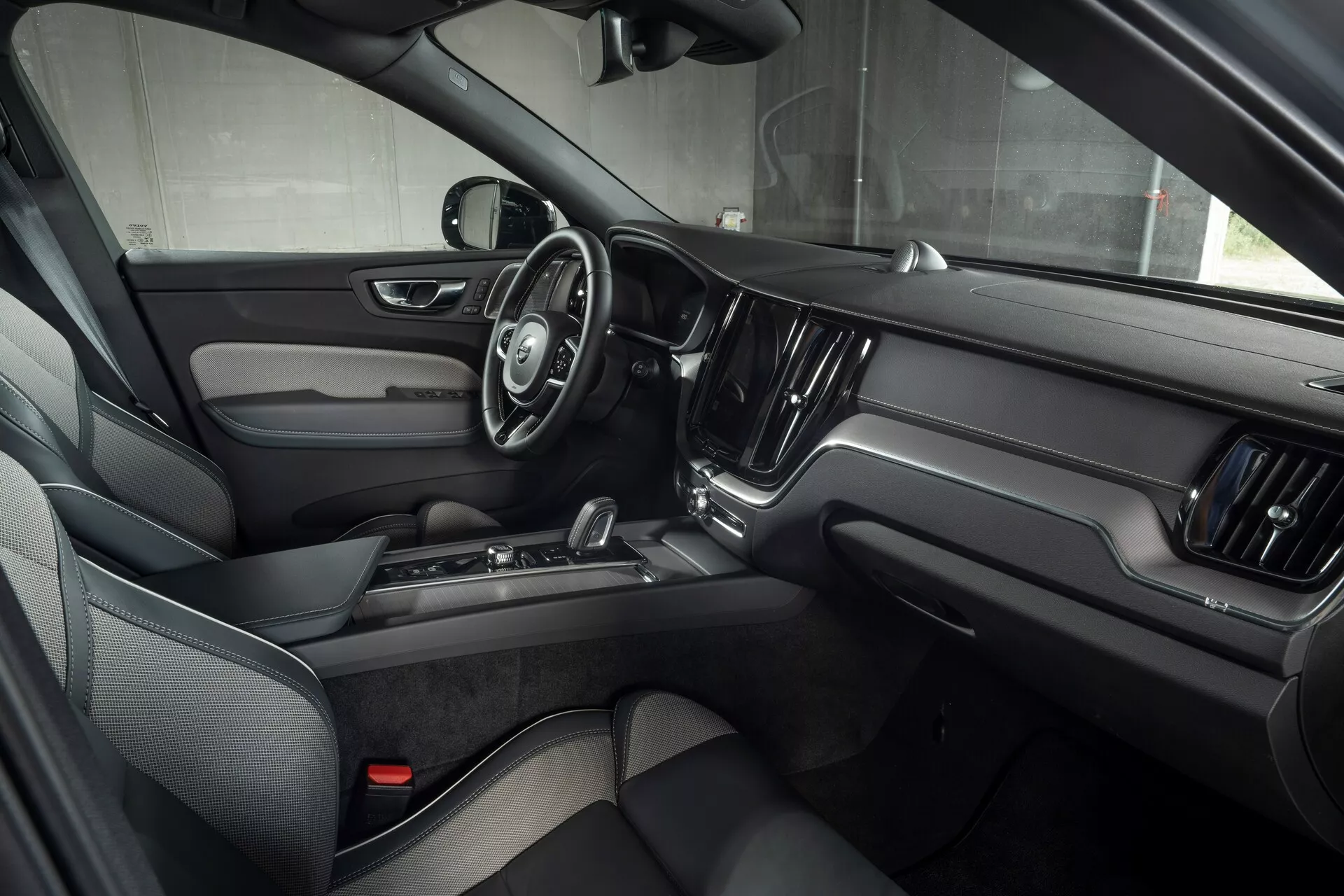 Interiörvy av Volvo XC60 2021 (2:a generationens ansiktslyft) från främre passagerarsidan, som framhäver förardörr med elektroniska kontrollsystem, treekrad ratt med multifunktionsknappar, stor central pekskärm för infotainment och lyxig design med mörkt läder och metalliska detaljer.