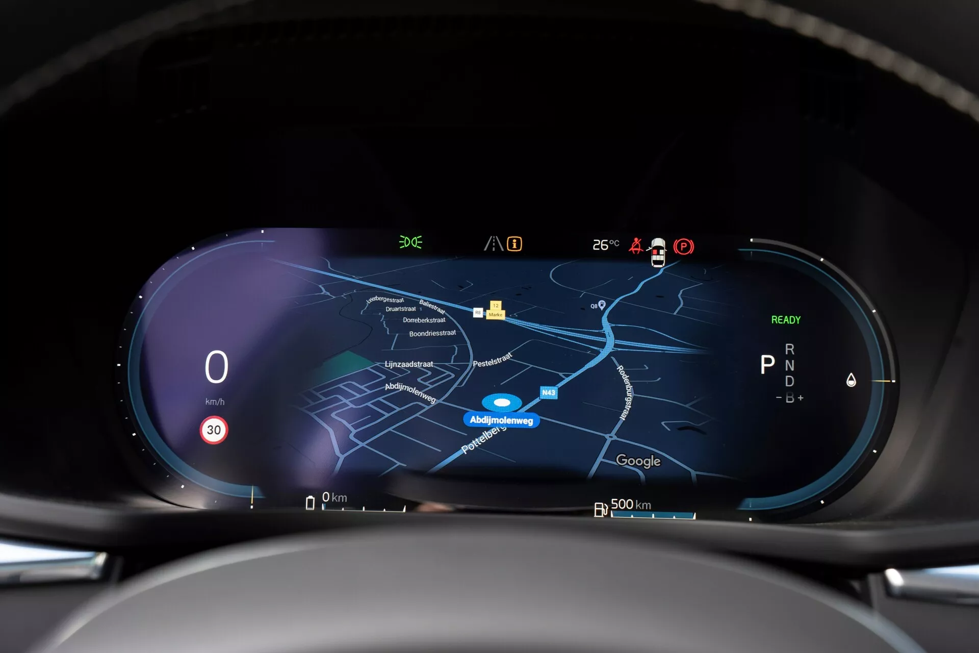 Interiörvy av Volvo XC60 2021 andra generationens facelift som visar en högupplöst digital instrumentpanel från förarens perspektiv. Panelen har en bredbildsskärm med en hastighetsmätare som visar noll, en växelindikator som visar 'P' och en central navigeringskarta i nattläge. Olika ikoner för signalmottagning, utomhustemperatur, batteriladdning och förarassistansfunktioner är synliga längs överkanten, vilket indikerar realtidsanslutning och avancerade tekniska kapaciteter.