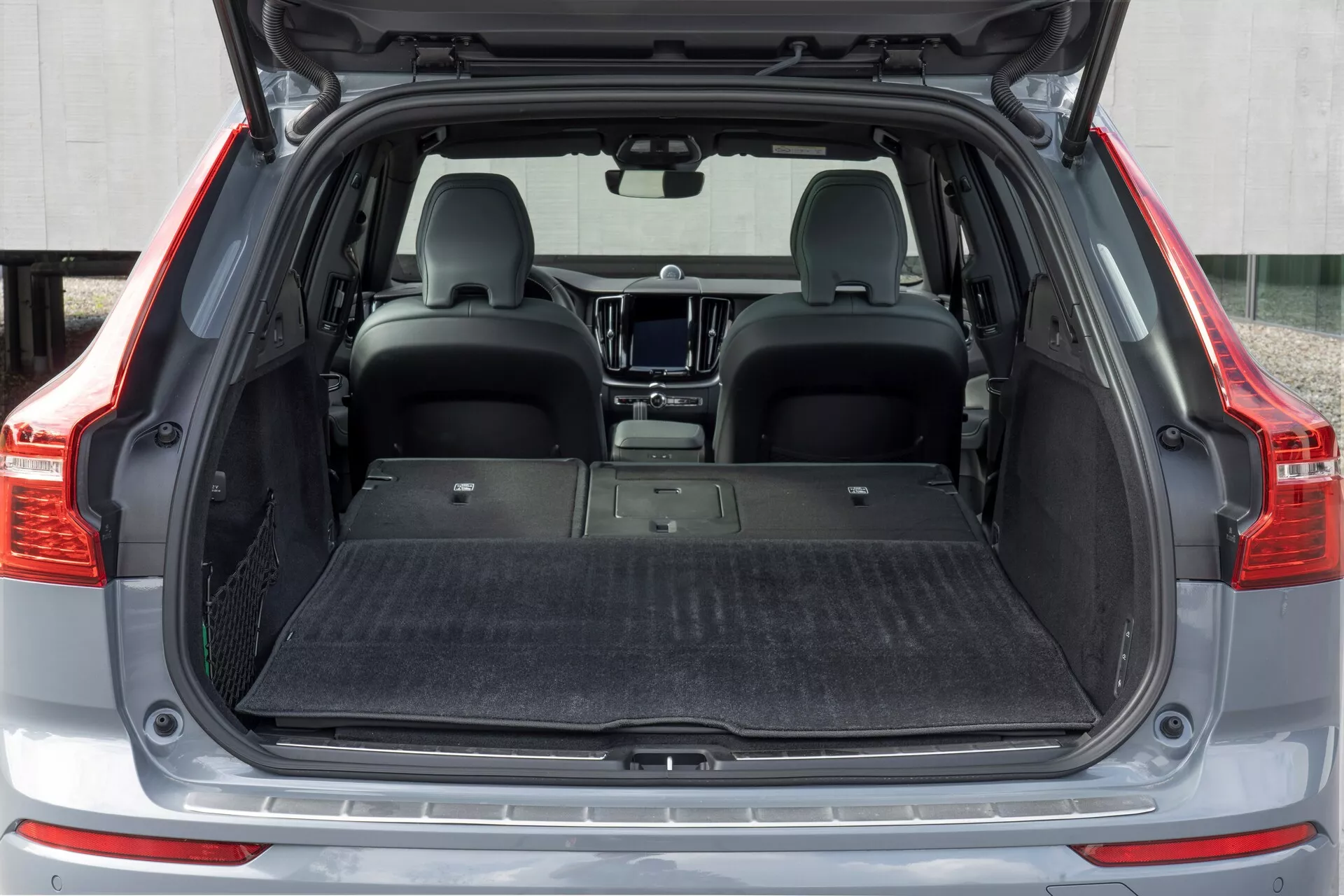 Lastutrymmet bak i en Volvo XC60 2021 (andra generationens facelift) från en rak bakåtperspektiv. Det öppna bagageutrymmet visar ett tomt, mattbelagt plant lastgolv, med nedfällda baksäten för ökad lagringskapacitet. Interiören är modern, med en skyddsmatta på golvet, men utan synliga organiseringsverktyg som lastnät eller krokar.