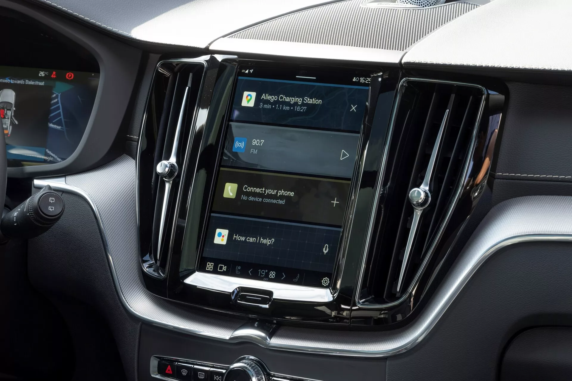 Interiörsbild av en Volvo XC60 2021 (andra generationens facelifting) med fokus på det centrala infotainmentsystemet. Den vertikalt orienterade skärmen, liknande surfplattor och smartphones, är inramad av metalliska luftventiler som antyder en högre modell. Under skärmen finns fysiska knappar och en vridknapp som indikerar en kombination av pekskärm och fysiska kontroller. Navigationsskärmen indikerar GPS-funktionalitet, med uppmaningar för telefonanslutning och röstkontroll, vilket tyder på funktioner som Bluetooth, röstigenkänning och smartphoneintegration. Tiden visas som 09:07. Bilden belyser infotainmentsystemets funktioner utan att visa varumärkes- eller modellidentifierare.