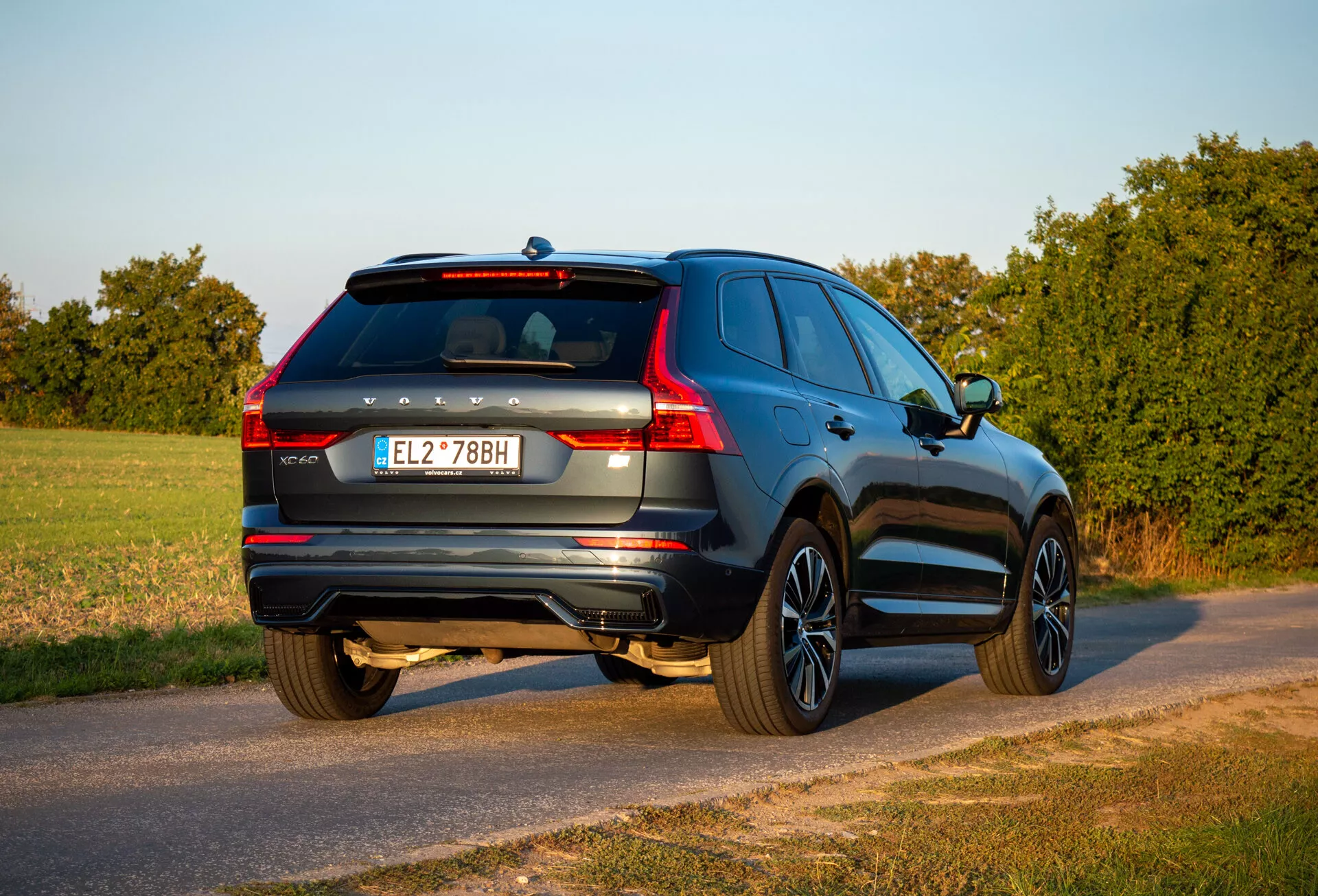 SUV Volvo XC60 Recharge plug-in hybrid 2021 i en tre fjärdedels bakifrån vy parkerad på en landsväg under guld timmen med synlig bakdel, passagerarsida, bagagelucka detaljer och designfunktioner