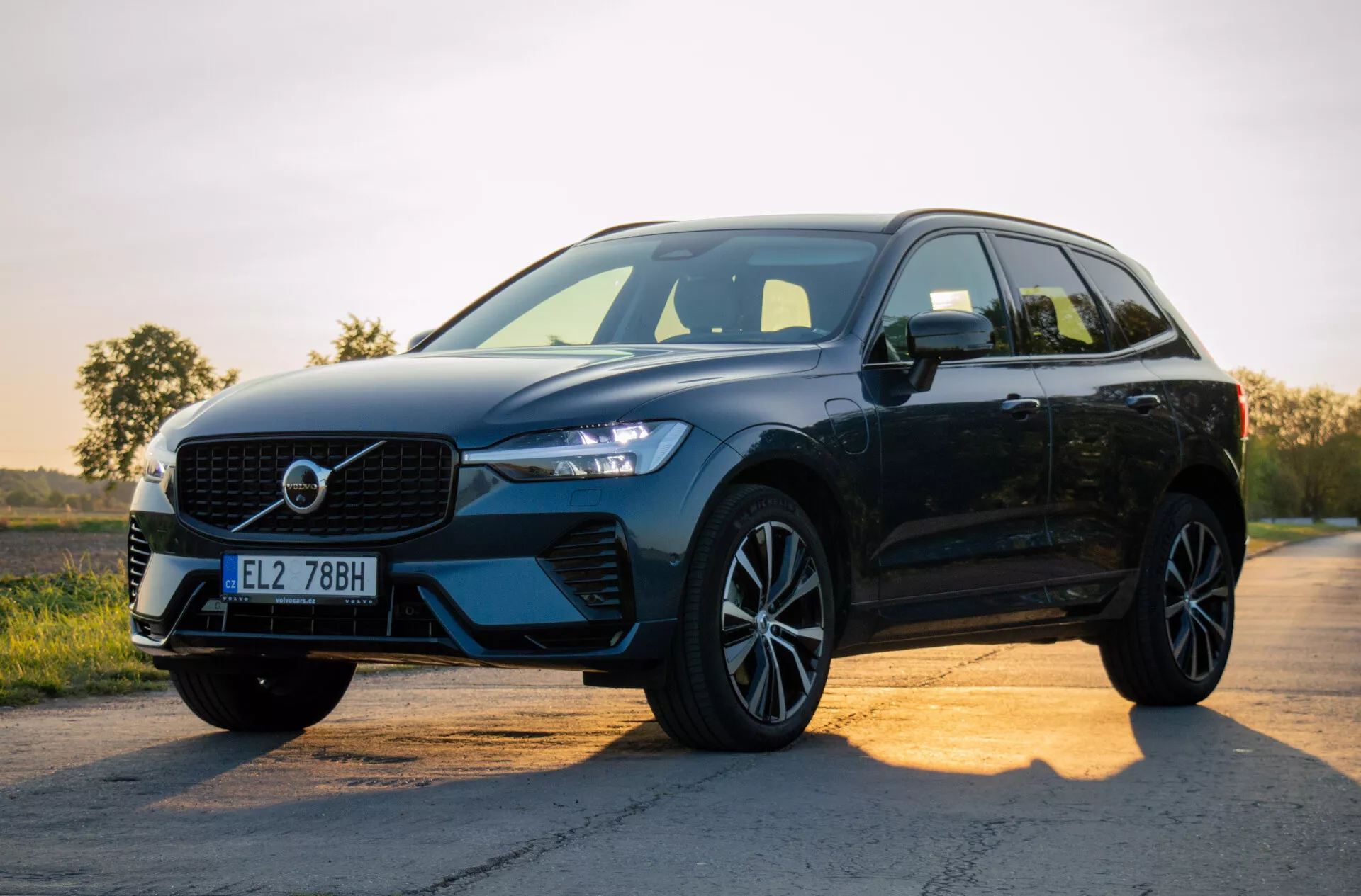 2021 Volvo XC60 Recharge Plug-in Hybrid, svart modernt SUV parkerad på en asfalterad väg vid soluppgång eller solnedgång, visar upp dess design med fokus på grillen, LED-strålkastare, legeringshjul och sidoprofil mot en gradient himmel bakgrund