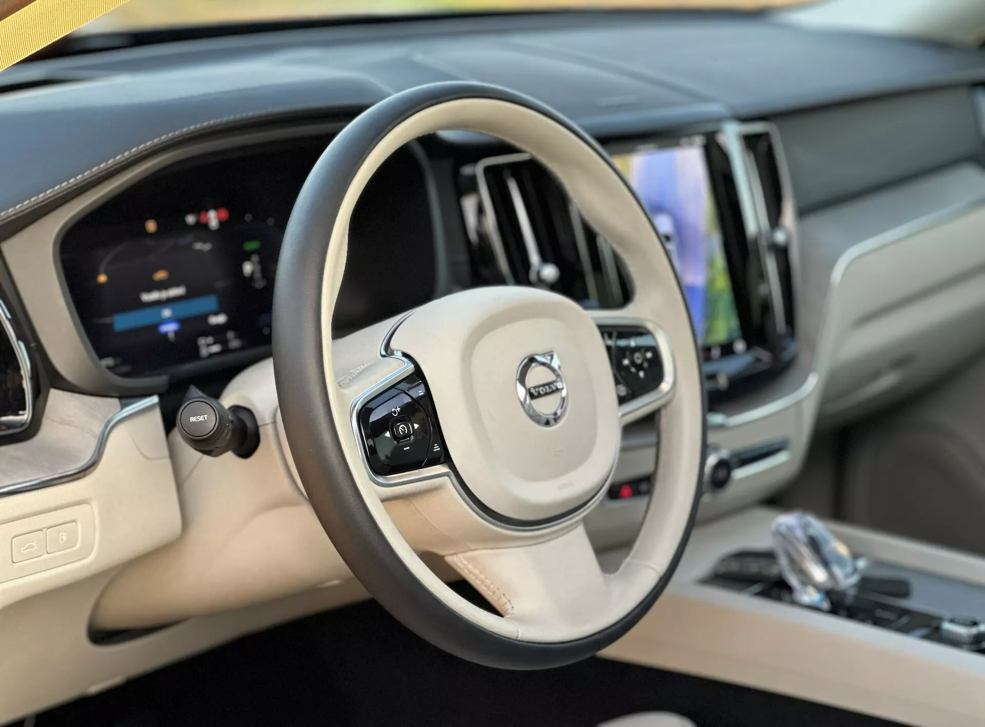 Interiörvy av Volvo XC60 Recharge Plug-In Hybrid 2021 från förarens perspektiv som visar ratten och den digitala instrumentpanelen, med betoning på farthållare, ljudstyrningsknappar, en pekskärmsinfotainmentsystem och lyxiga material