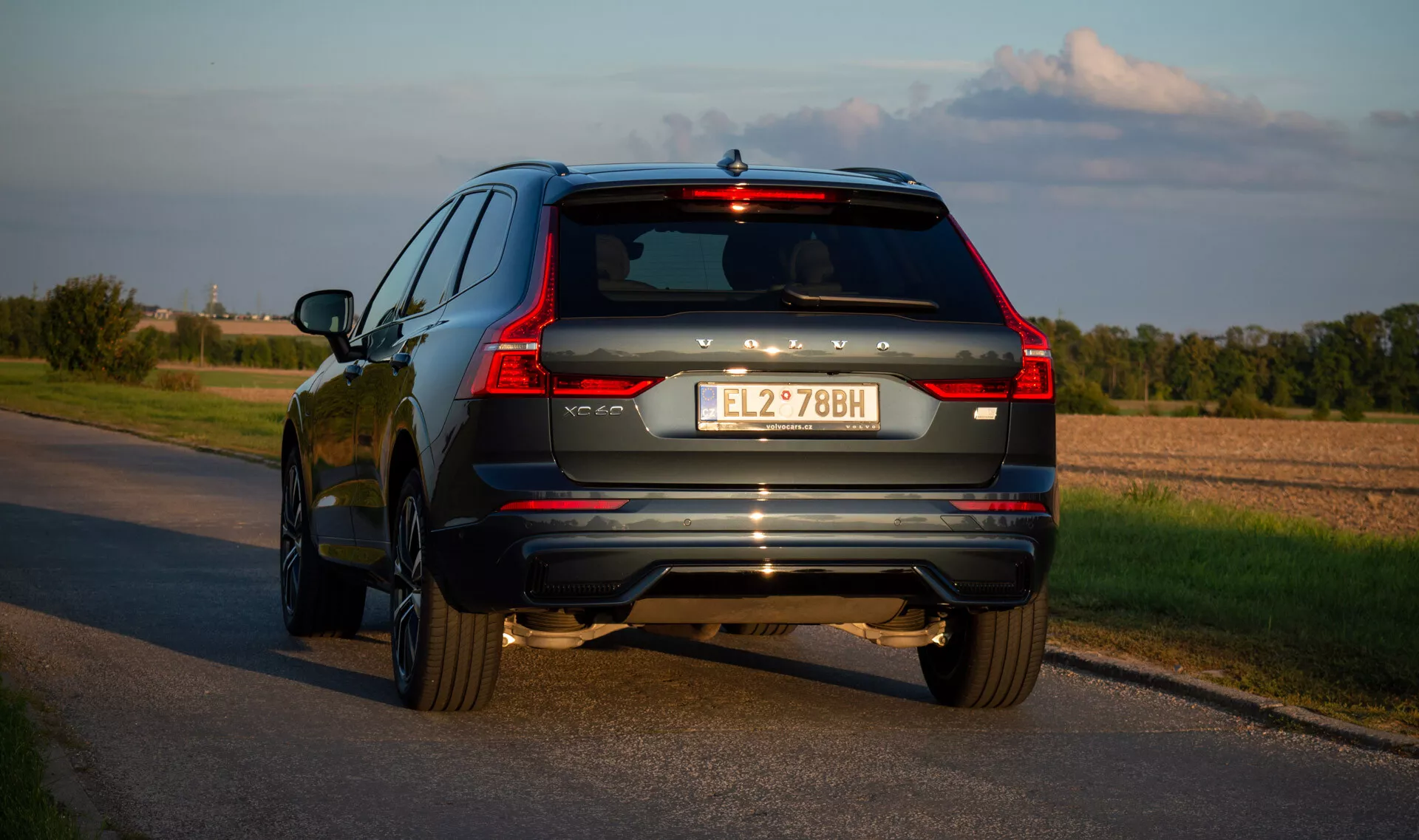 2021 Volvo XC60 Recharge plug-in hybrid SUV på asfalterad väg, fångad från ett bakre trekvarts perspektiv som belyser fordonets LED-bakljus, avgassystem och kromdetaljer under sen eftermiddag