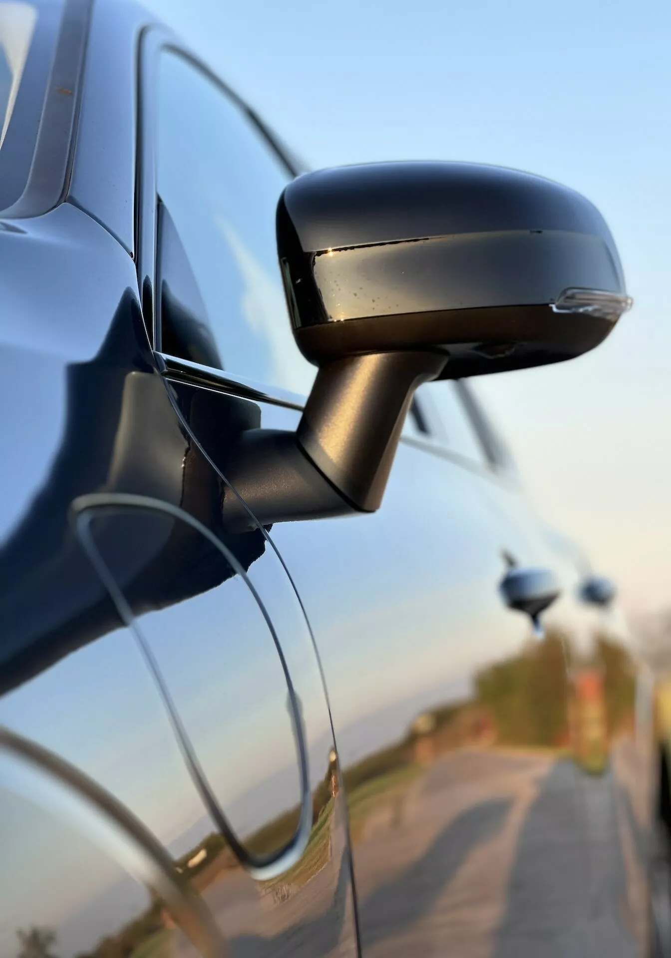 Närbild av Volvo XC60 Recharge Plug-In Hybrid 2021:s sidospegel som visar dess slanka design, integrerade blinkers och fäste till bildörren, vilket belyser fordons teknik och säkerhetsfunktioner.