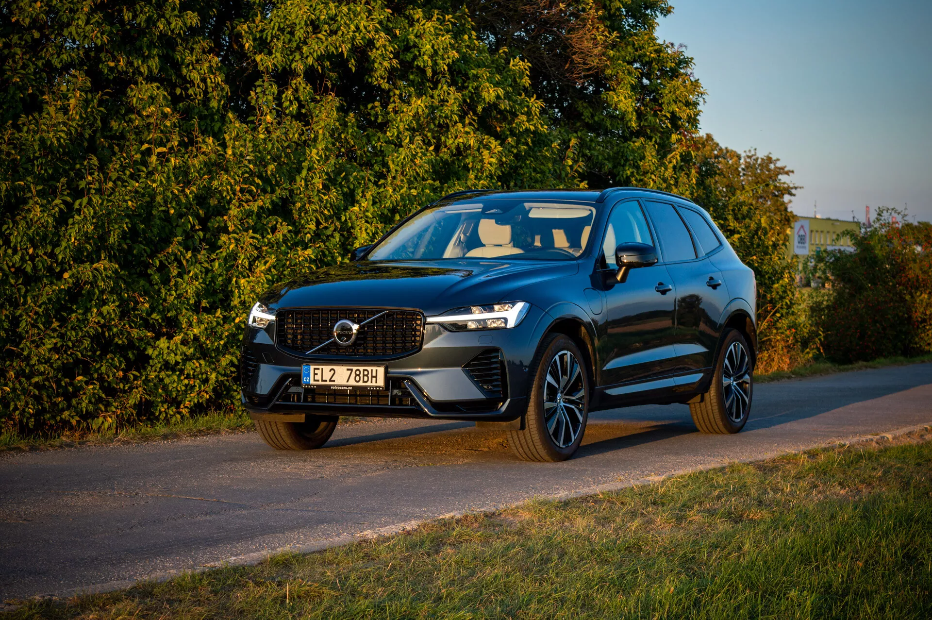 2021 Volvo XC60 Recharge Plug-In Hybrid parkerad vid vägkanten under sen eftermiddag med varmt ljus, visar frontgrillen, LED-strålkastare och sportig profil mot en bakgrund av vegetation