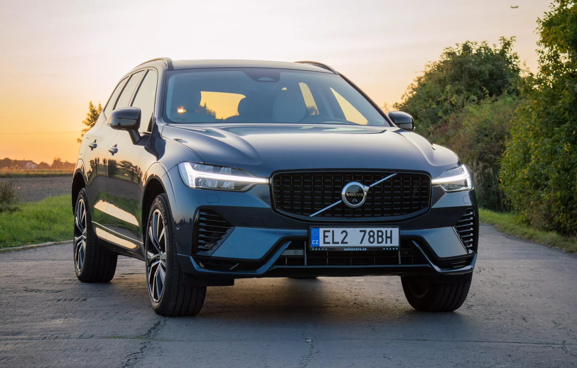2021 Volvo XC60 Recharge Plug-In Hybrid lyxig SUV på asfalterad väg med naturlandskap under gyllene timmen, med frontgrill, LED-strålkastare, skulpterad huva, flerspakiga legeringshjul och blank yta