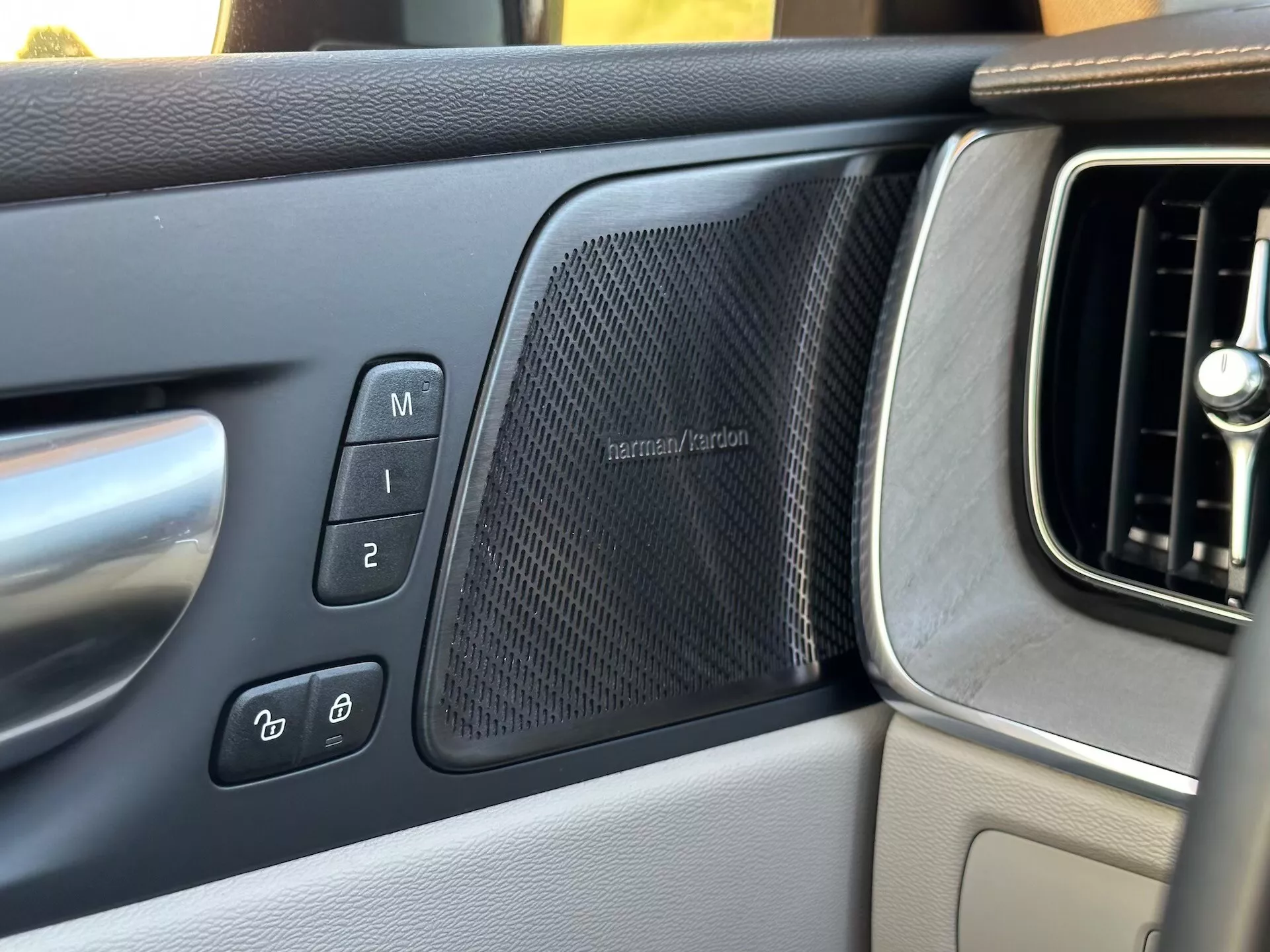 Interiörvy av Volvo XC60 Recharge Plug-In Hybrid 2021 med fokus på förarsidans dörrpanel som visar minnessätesinställningar, elektronisk dörrlåskontroller, en harman/kardon-högtalargaller och en del av instrumentbrädans ventilationsgaller