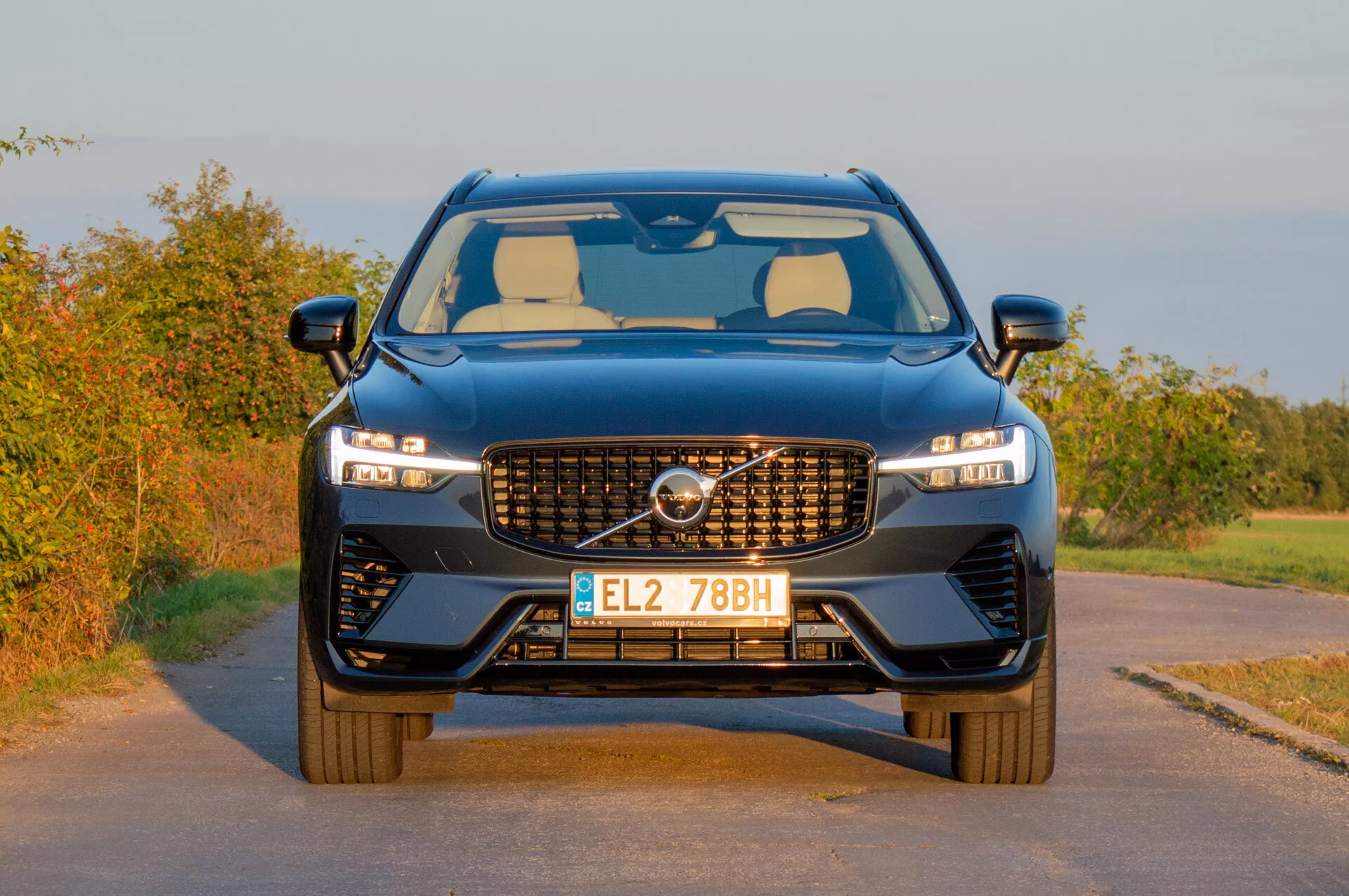 Volvo XC60 Recharge Plug-In Hybrid 2021 som visar upp sin moderna design med ett distinkt grill, smidiga LED-strålkastare och en sportig frontspoiler mot en lantlig bakgrund i sen eftermiddags varma belysning