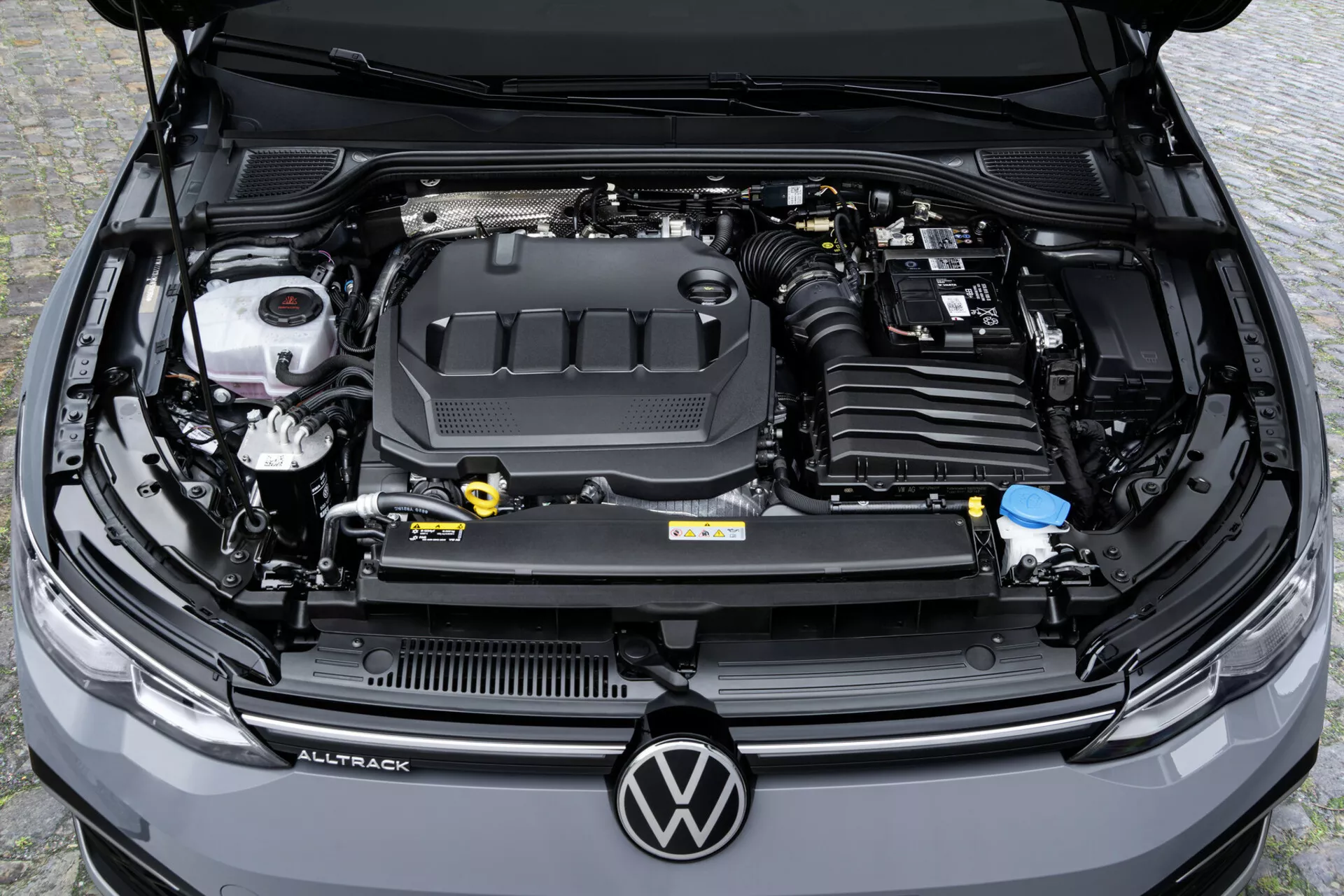 Översikt från ovan på motorutrymmet i en Volkswagen Golf Alltrack 2017 som visar motorlocket med logotyp, vätskebehållare och bilbatteri