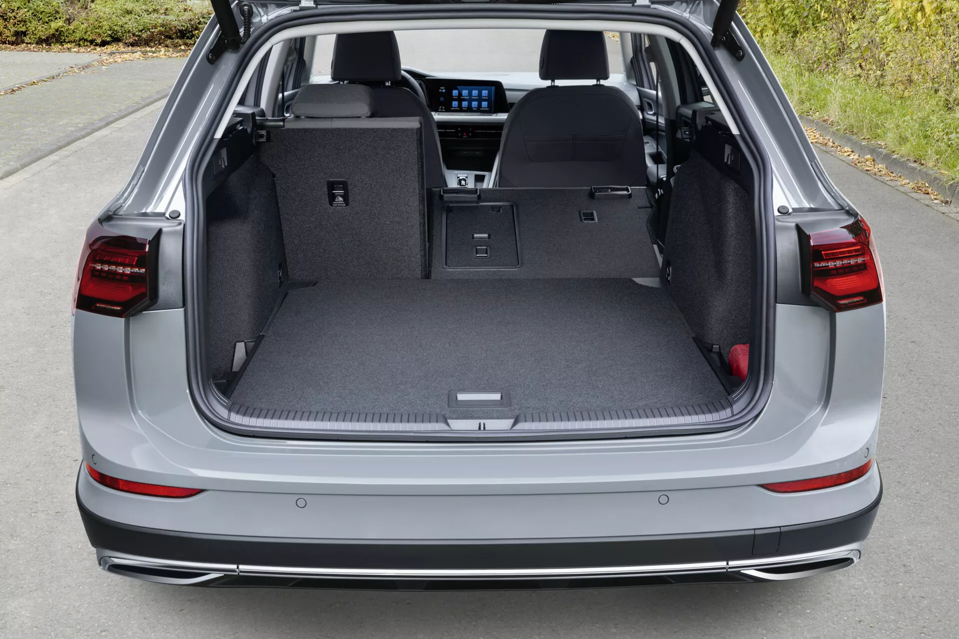 Bakre lastutrymmet i VW Golf Alltrack 2017 med öppet bagageutrymme och nedfällda baksäten, ljusgrå interiör, skyddsmatta, infälld handtag, lastfack och en glimt av avancerade interiörfunktioner