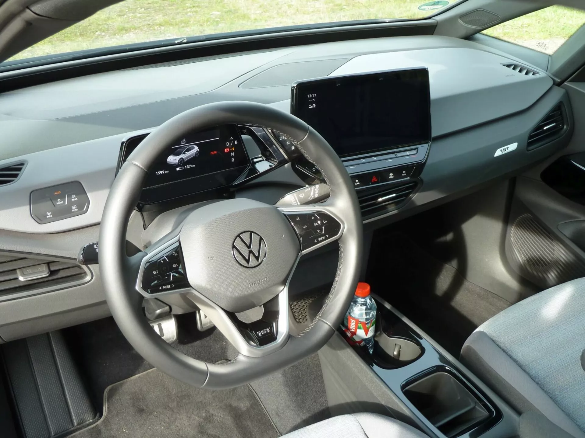 Modern interiör av VW ID3 2020 med digital instrumentpanel och förhöjd fram-höger vy av förarens cockpit med framträdande centrerad ratt som visar Volkswagen-emblemet, inbyggda kontroller och pekskärmsförsett infotainmentskärm