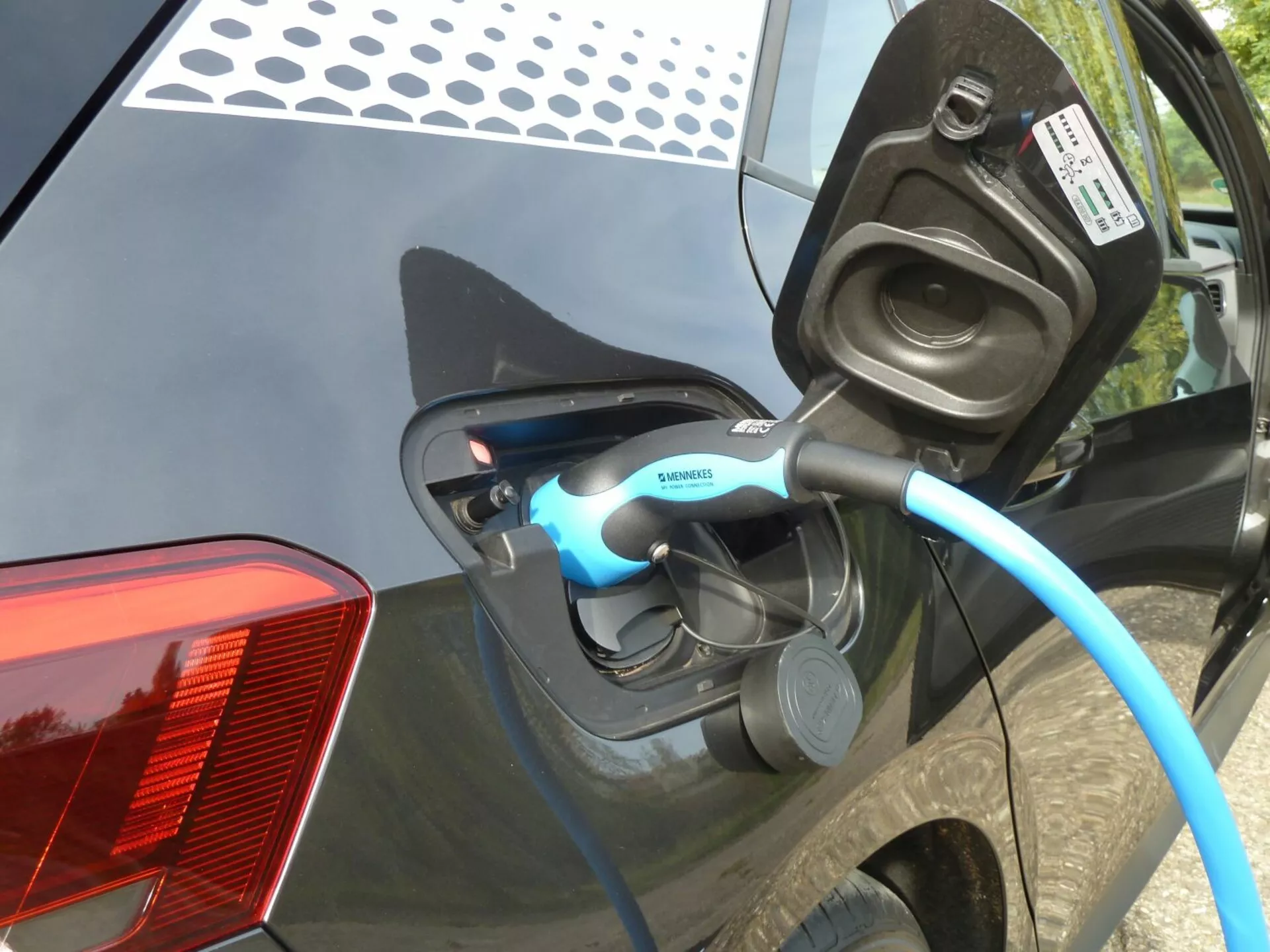 Närbild på laddningsprocessen för en VW ID.3 elbil från 2020, fokuserad på den öppna laddningsporten och Siemens-märkta kabeln vid bilens bakre kvartspanel, med synlig LED-indikator och detaljerade funktioner som den moderna LED-baklyktans design och den glansiga mörkfärgade karossen.