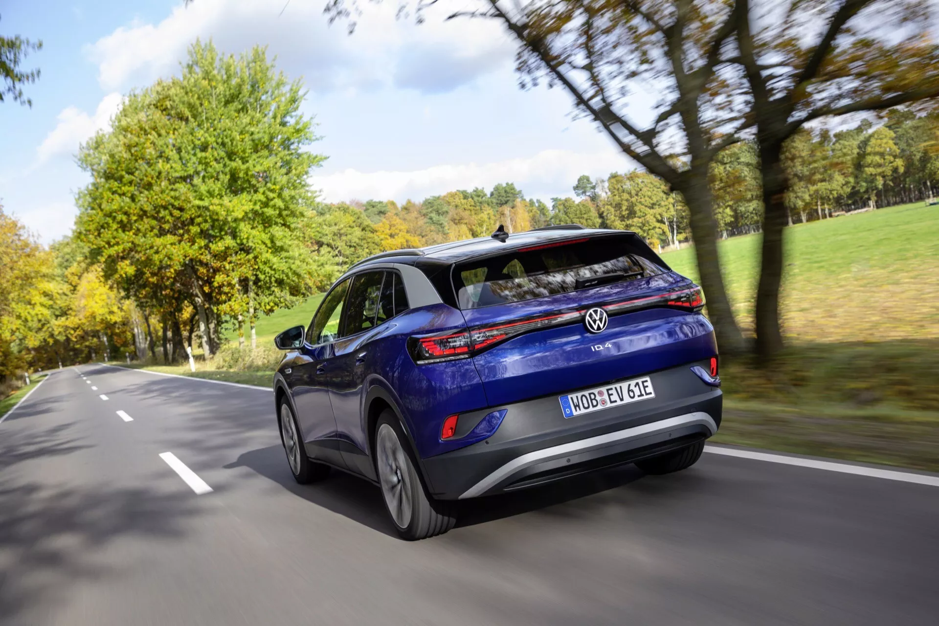 VW ID.4 1:a generationen från 2020 i rörelse, avbildad från ett trekvarts baksida perspektiv som visar dess aerodynamiska blåa hatchback-design, LED-bakljus, och legeringshjul på en tvåfilig väg med rörelseoskärpa effekt.