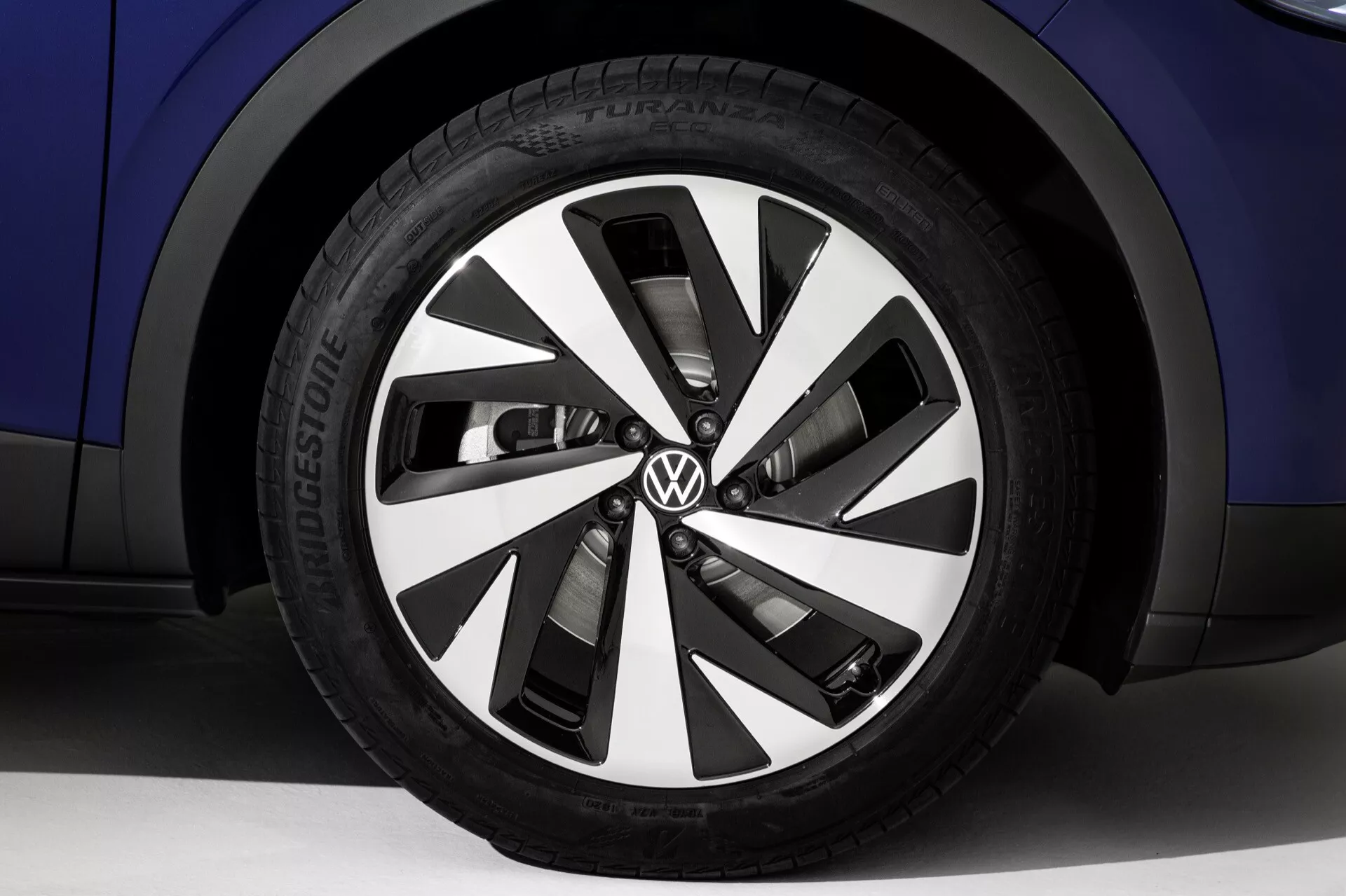 Närbild av hjulet på Volkswagen ID.4 första generationen från 2020 med en stilren legeringsdesign i svarta och silverområden, Bridgestone-däck och synlig Volkswagen-logotyp mot en blå karossbakgrund