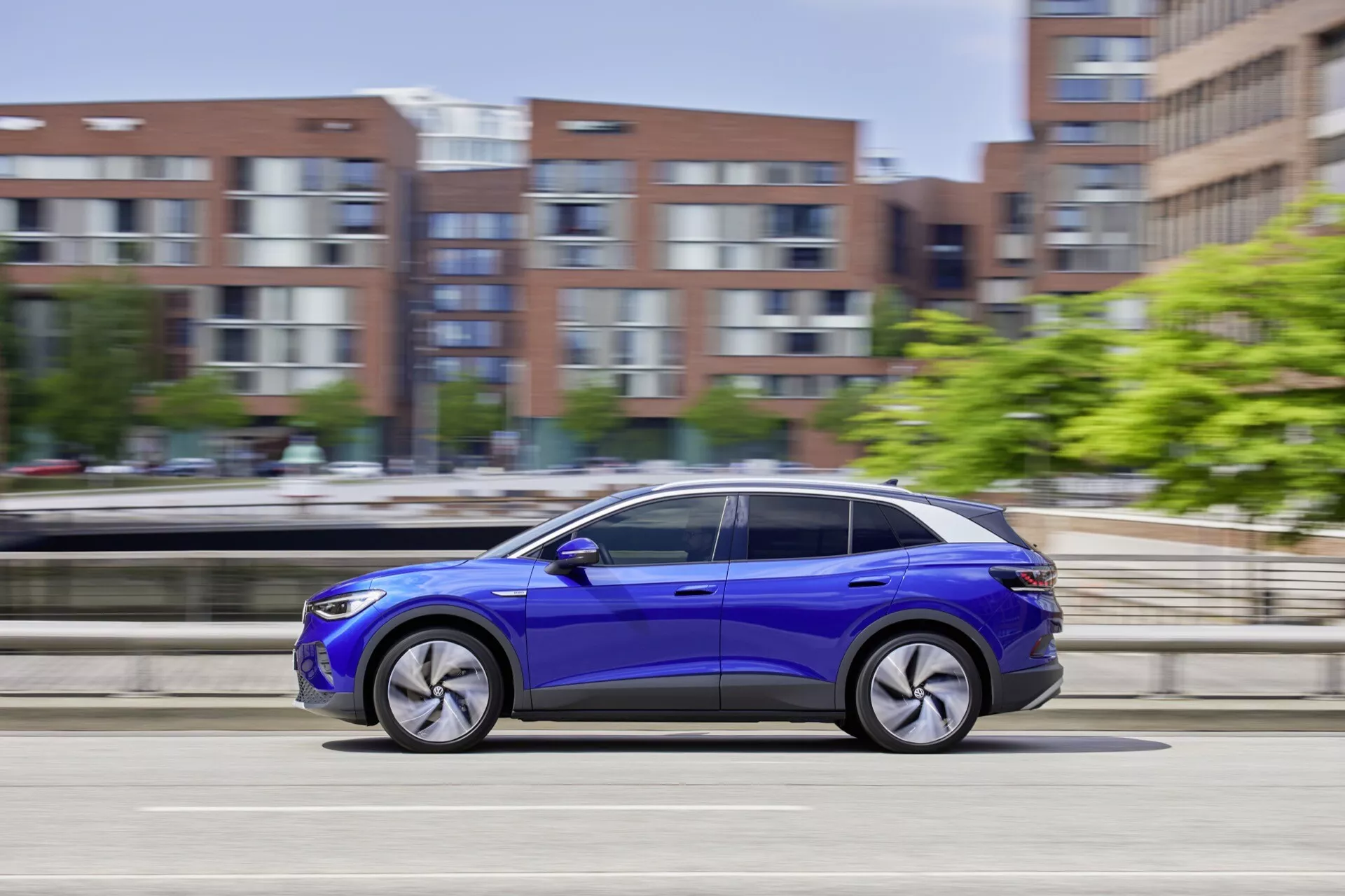 Dynamisk sidoprofil av en VW ID.4 2020 i rörelse, som visar upp livlig blå färg, legeringshjul och moderna designfunktioner mot en suddig bakgrund