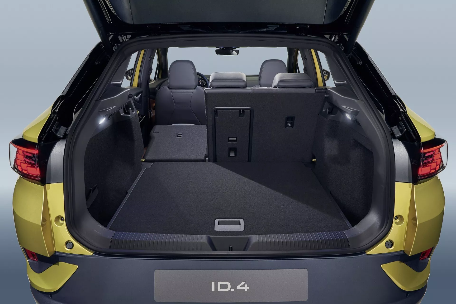 Baksida vy av en metallisk gul Volkswagen ID.4 från 2020 med öppen bagageutrymme som visar rymlig lastutrymme, detaljerad interiördesign och fällbara baksäten för utökat förvaringsutrymme, fångad från ett mellanmått perspektiv