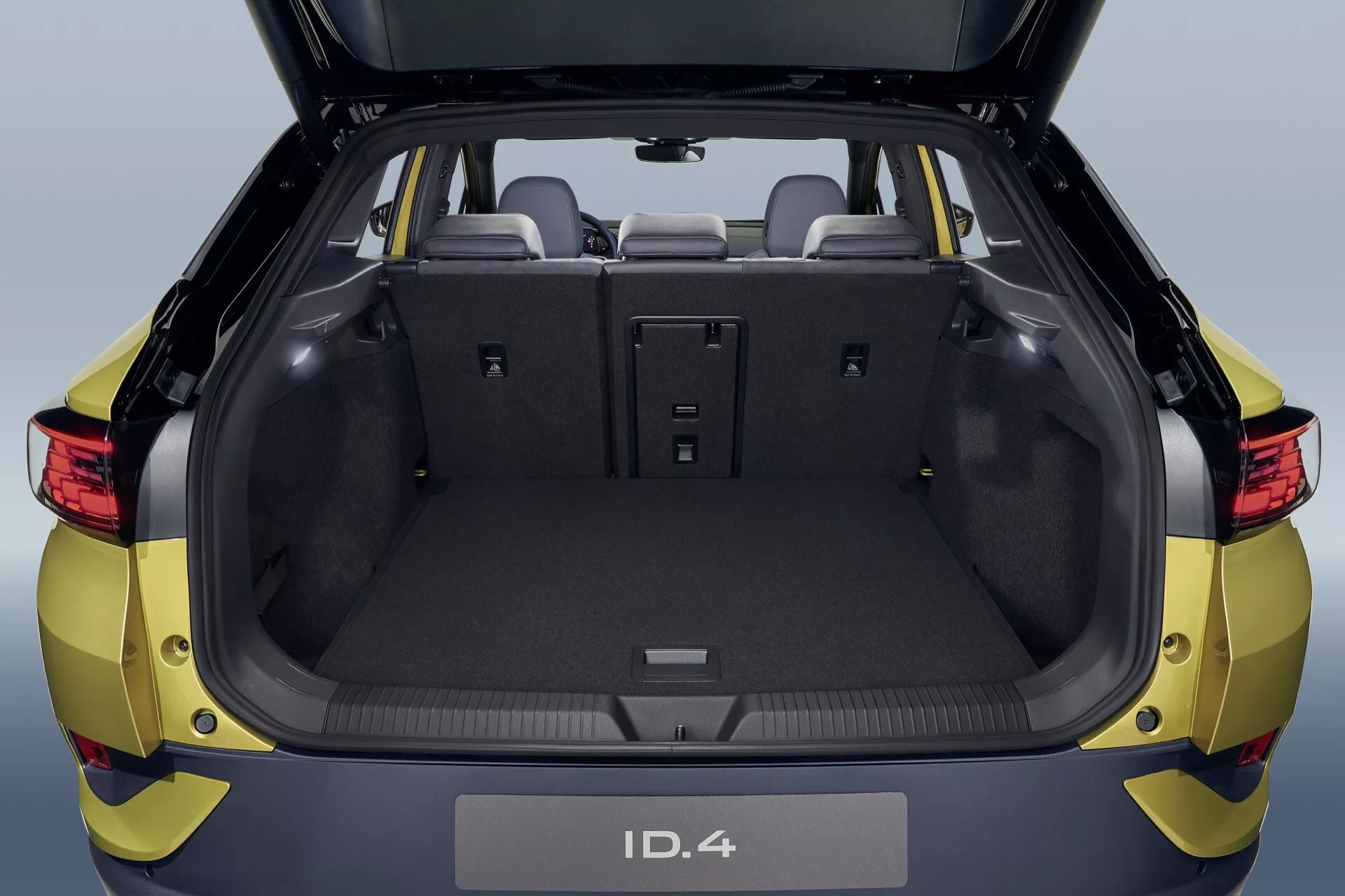 Volkswagen ID.4 från 2020 visar ett rymligt bagageutrymme med öppen lucka, framhäver baksitsar delbara i förhållandet 60/40 och en modern, ren design utan avgasutsläpp vilket indikerar dess elektriska fordonsegenskaper, med fokus på praktisk förvaring och lastkapacitet från ett baksiktsperspektiv.