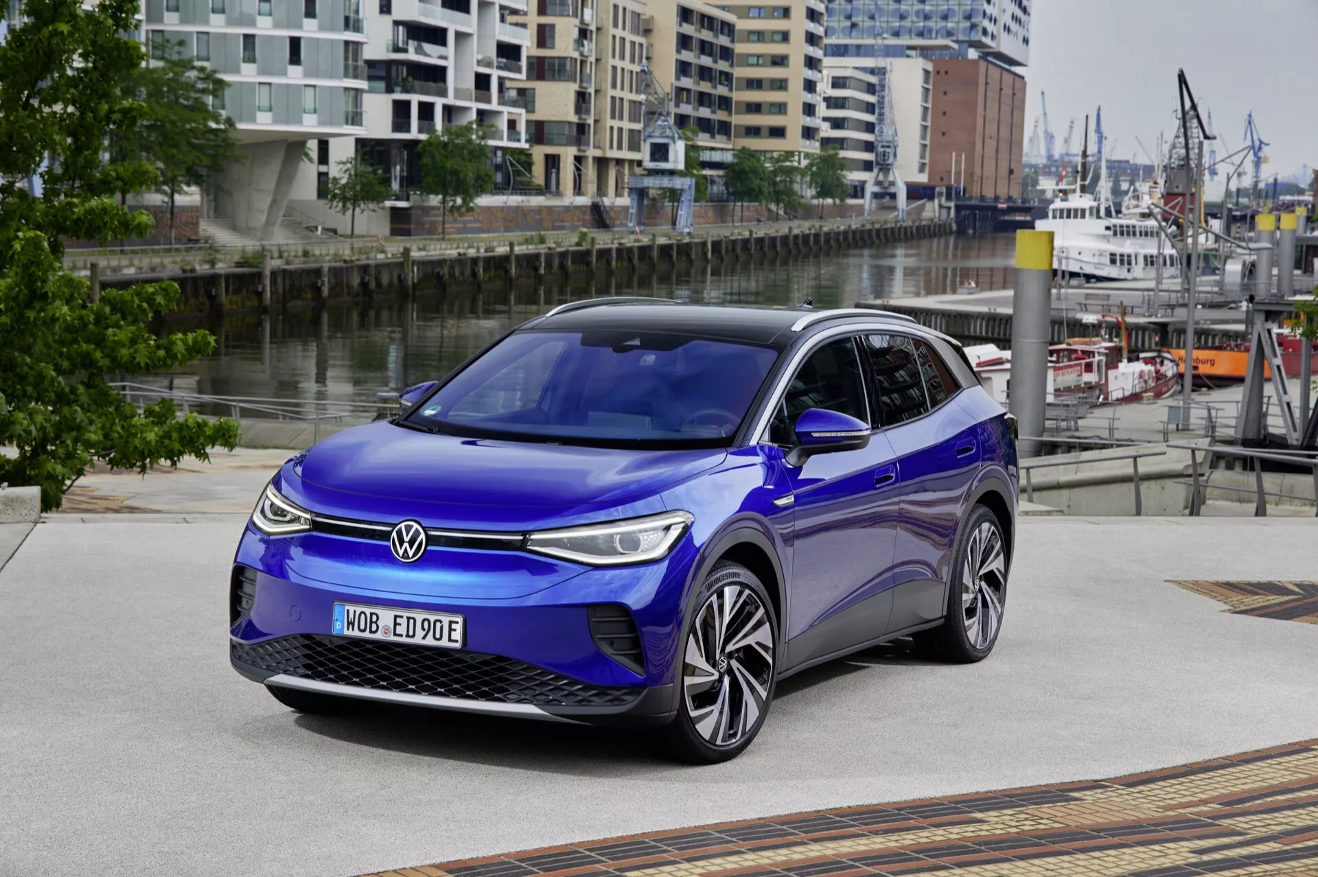 VW ID.4 första generationen 2020 med fokus på frontgrillen, motorhuven, den vänstra sidoprofilen och taket, med betoning på strålkastarnas design, aerodynamisk design och LED-teknik, placerad på ett mönstrat stadsdriv mot en arkitektonisk bakgrund