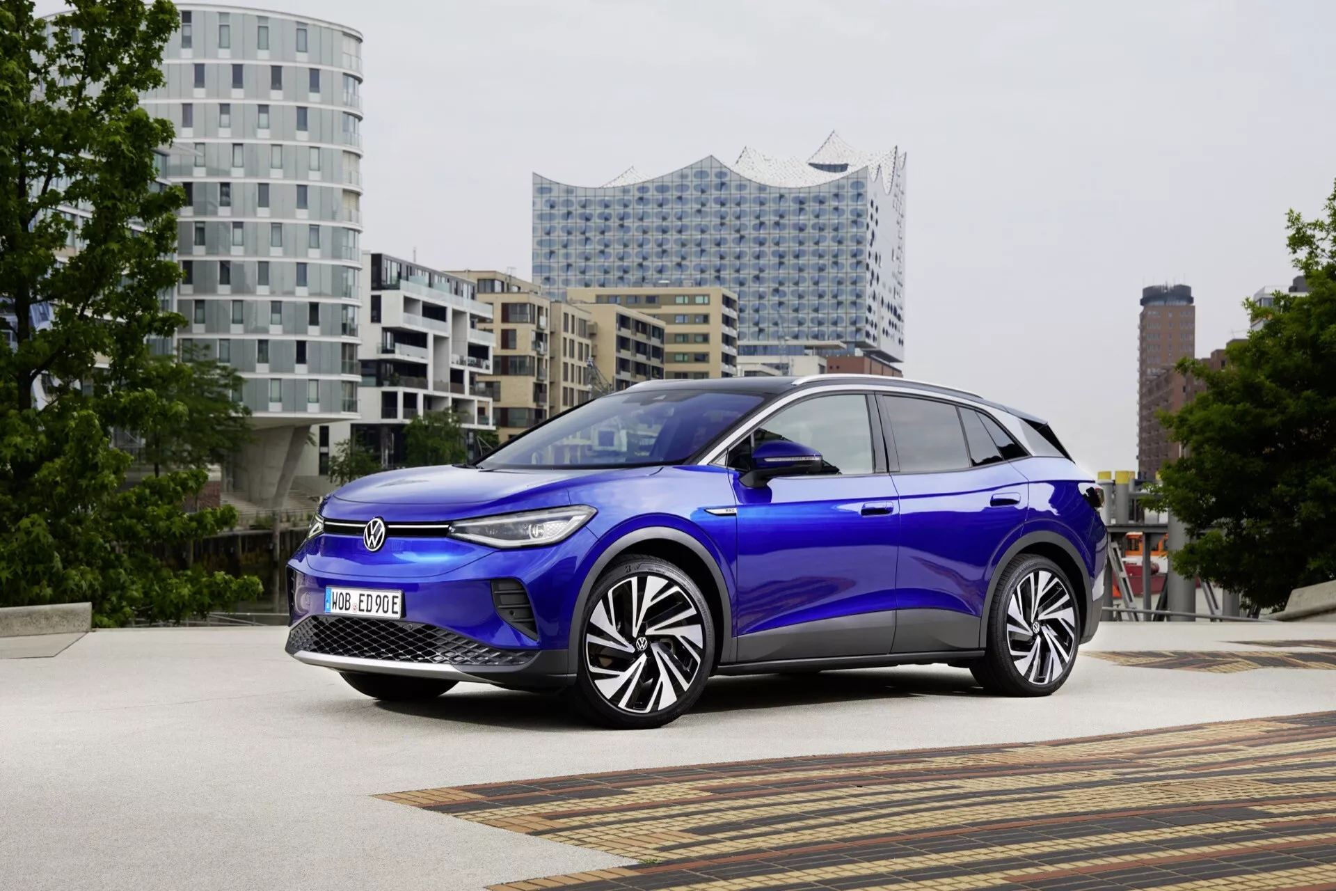 VW ID.4 1:a generationen 2020 i blått, visas från ett trekvartsfrontal perspektiv som visar frontgrillen, LED-strålkastarna, aerodynamiska karossen och moderna hjuldesign mot en urban bakgrund