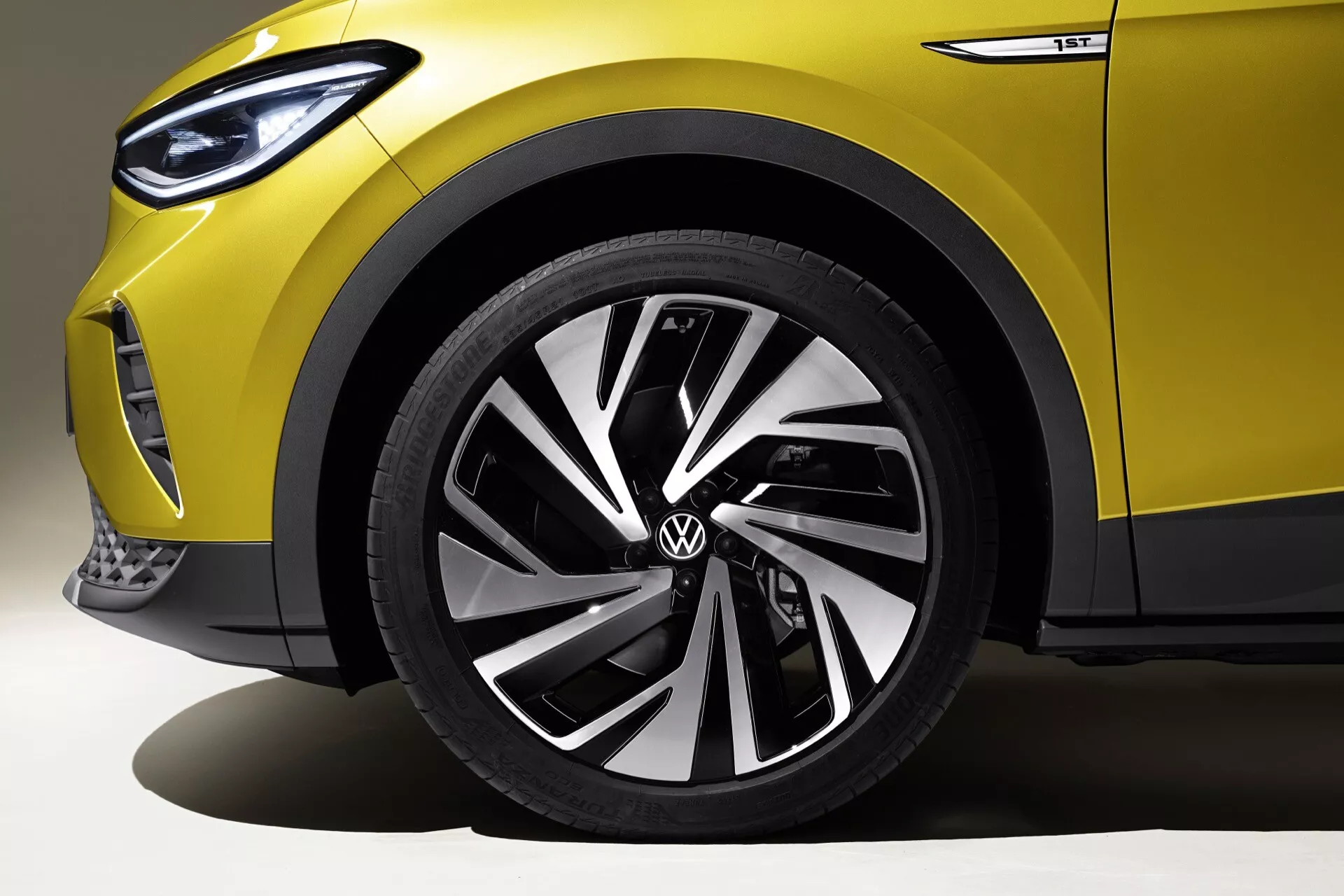 Detaljerad vy över Volkswagen ID.4 2020s framhjul och partiell sida, som visar flerspakig fälgs design och lågprofil däck i en studioinställning, med kontrollerad belysning som framhäver bilens moderna konturer, logotyp och avancerad strålkastarteknik.