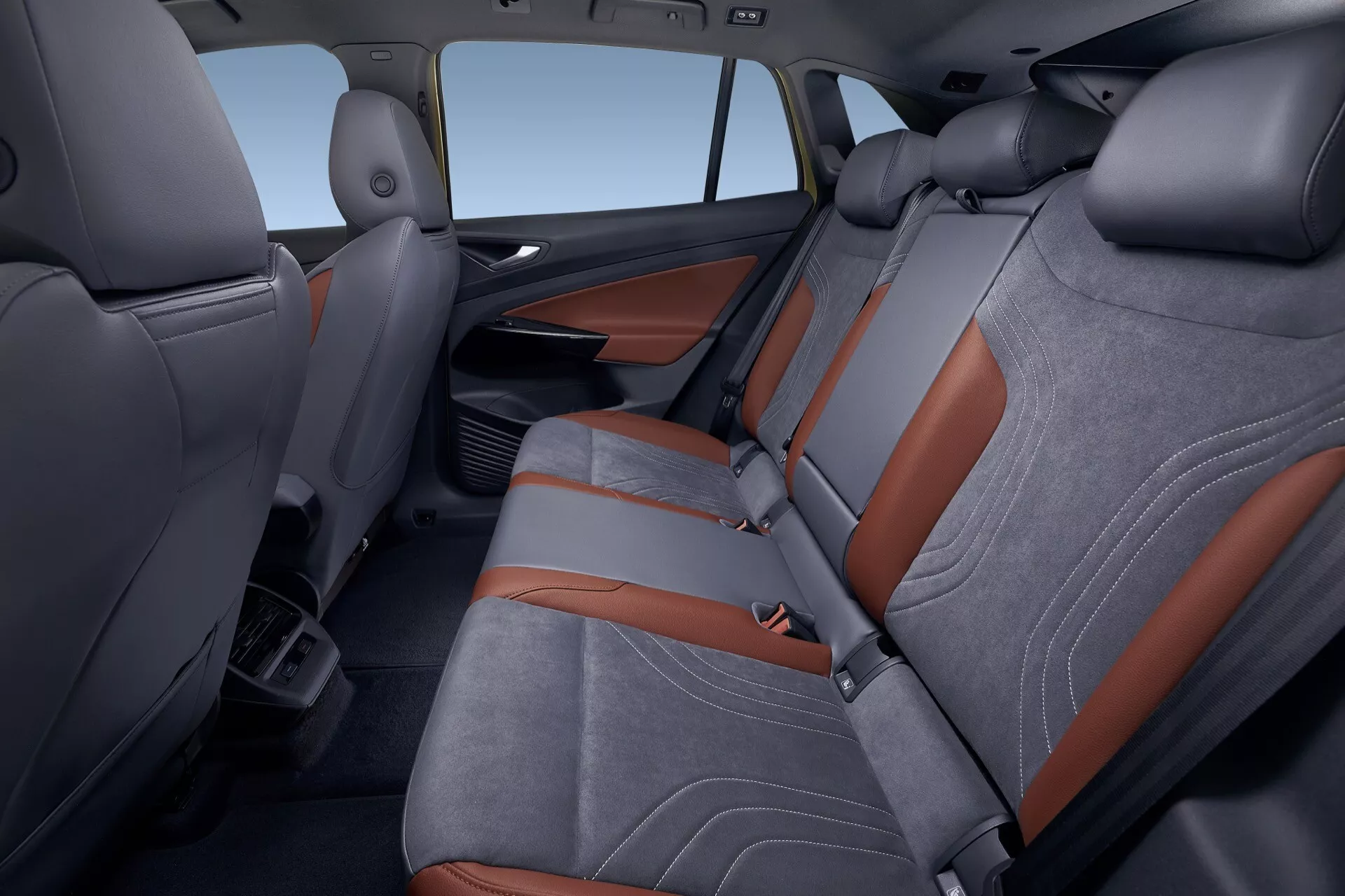 2020 VW ID.4 1:a generationens interiör som visar baksätesområdet från en ovanifrån mellanvinkel, fokuserad på passagerarsidan med tvåtonig klädsel och orange accenter, nedfällbar armstöd med mugginnehavare och synliga förvaringslösningar.