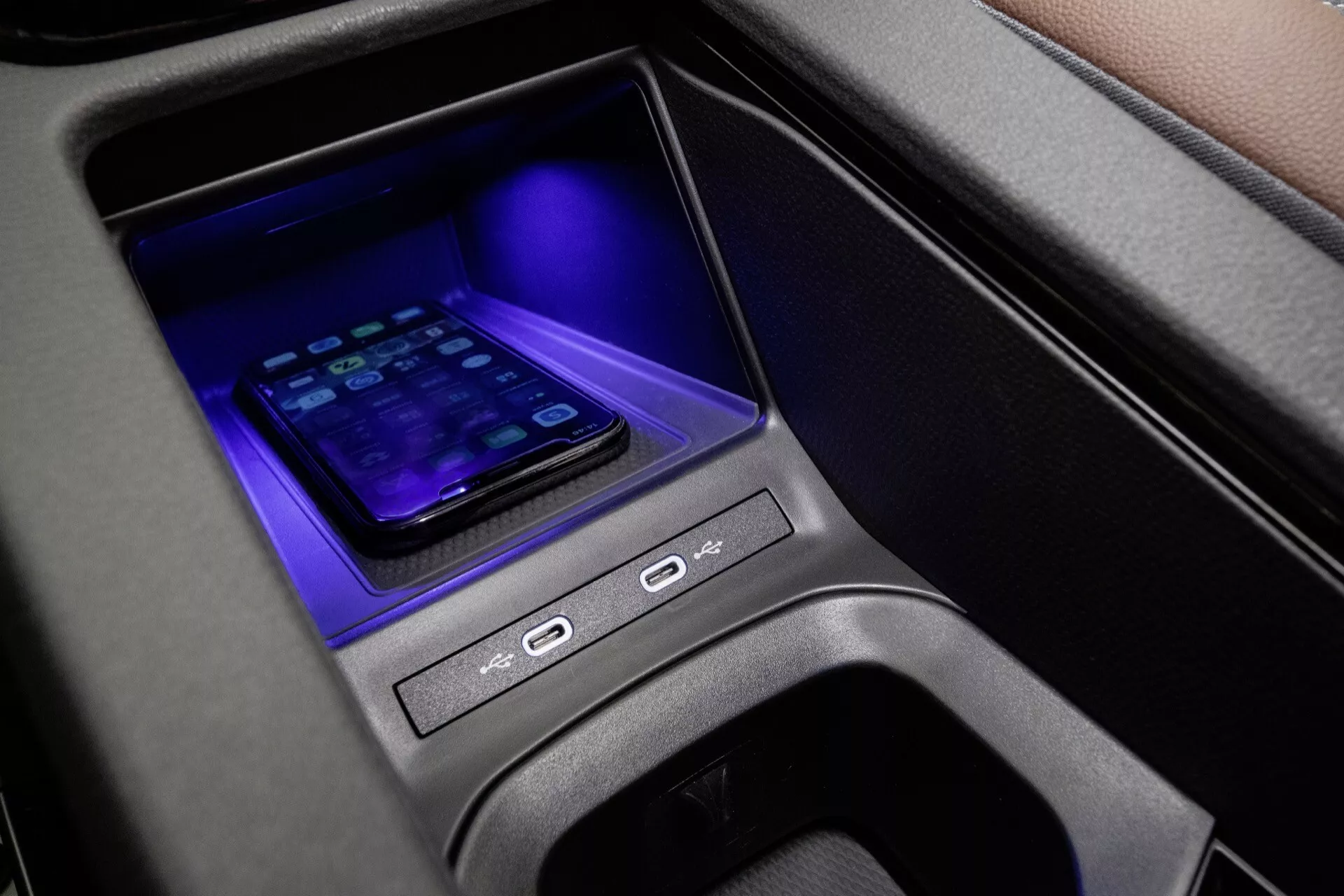 Närbild av mittenkonsolen i VW ID.4 2020 första generationen med trådlös smartphone-laddningsplats, blått omgivningsljus, kontrollknappar och modern anslutningsförmåga i en högkvalitativ interiör