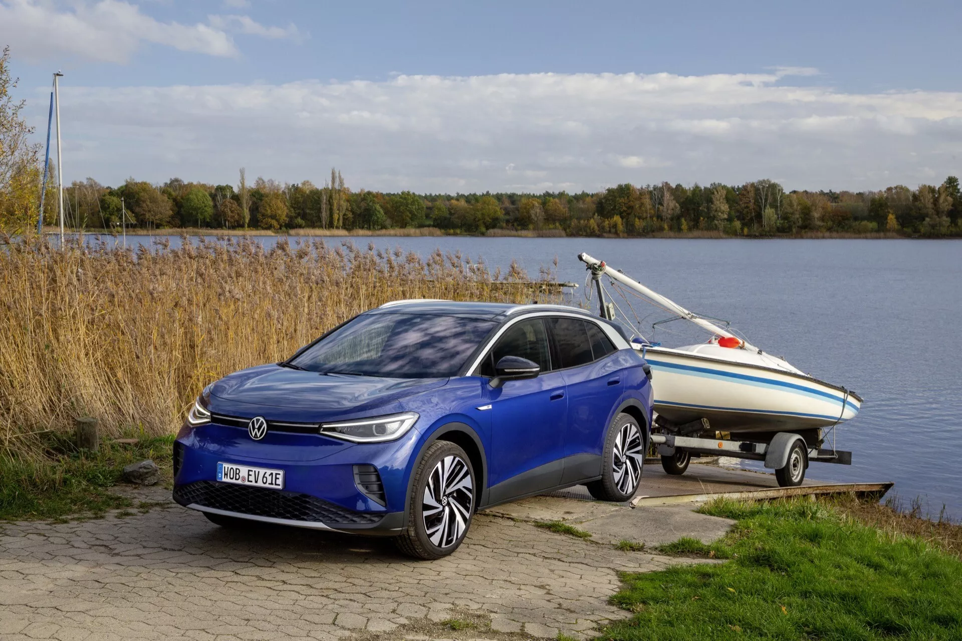 VW ID.4 1:a generationen från 2020 i en utomhusmiljö som bogserar en båt, framhävd av ett ¾ frontperspektiv som visar dess snygga, elektriska eller hybrid hatchbackdesign, LED-strålkastare, legeringshjul och placerad nära en vattenkropp med en fridfull naturbakgrund
