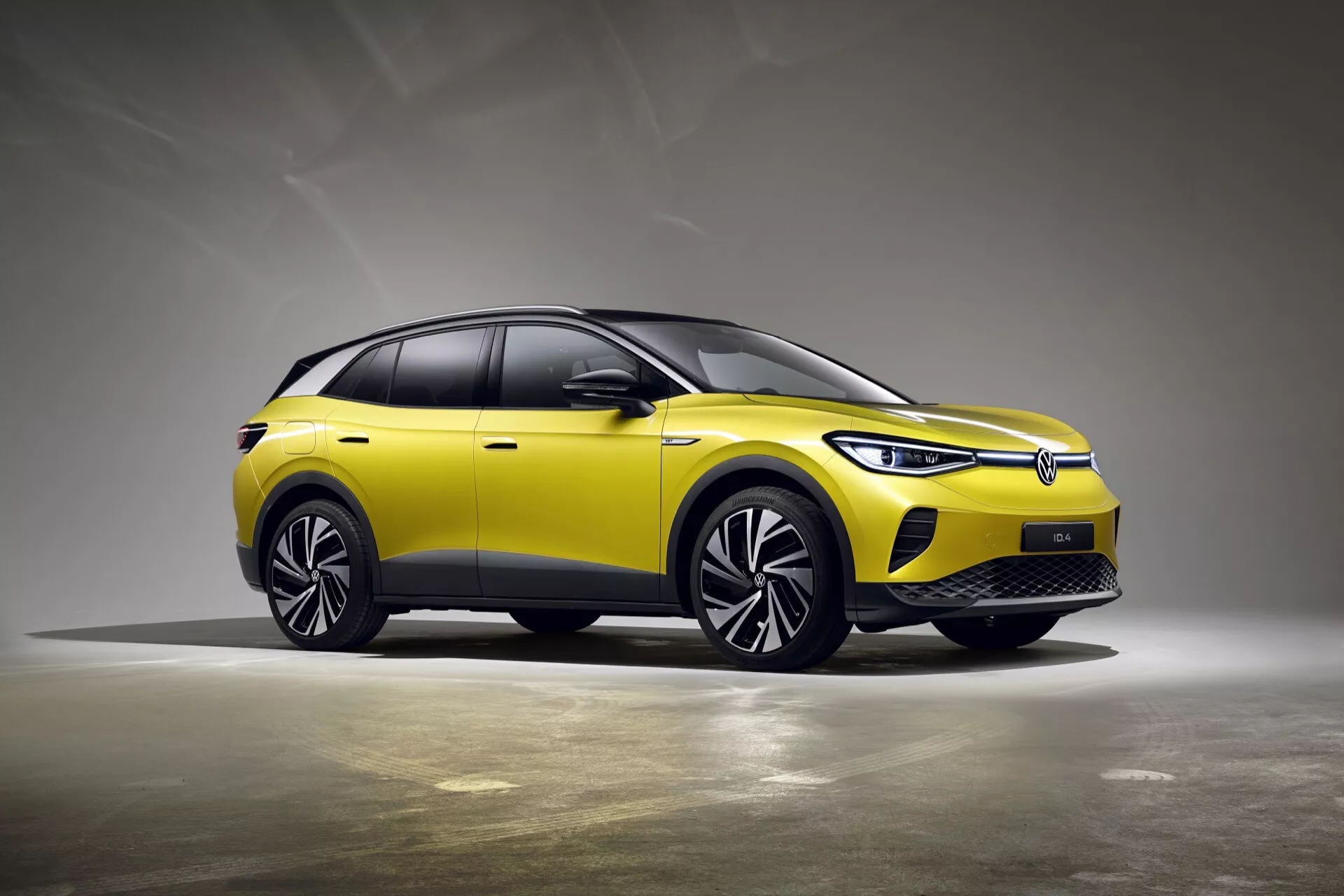 Trekvarts framsida av en gul VW ID.4 1:a generation crossover SUV 2020 i studioinställning med neutral grå bakgrund som framhäver dess slutna grill, LED-strålkastare, aerodynamiska hjul och slanka designfunktioner