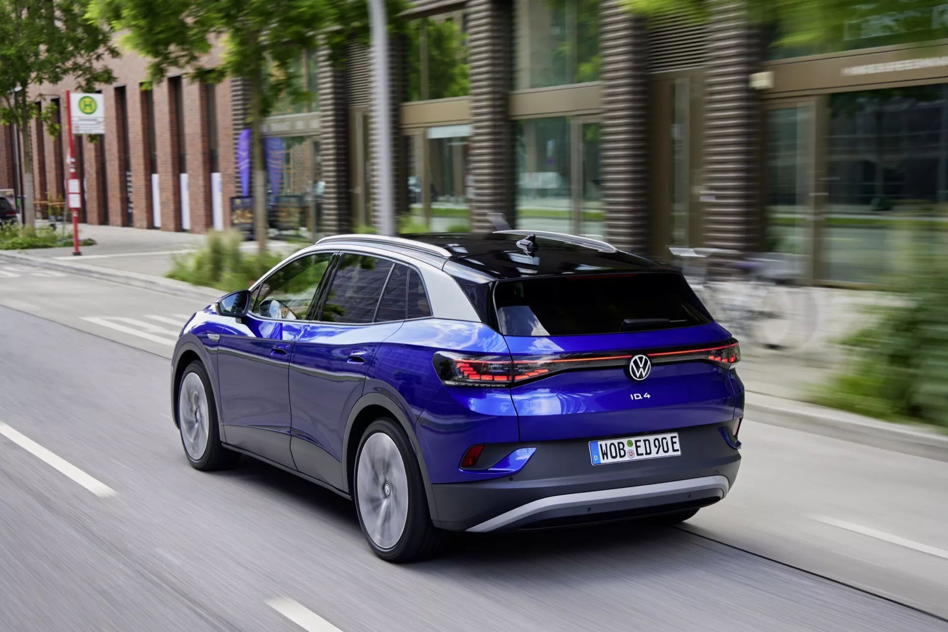 Dynamiskt bakre trekvartsutsikt av en blå Volkswagen ID.4, helt elektrisk SUV, i rörelse på en stads gata som markerar dess högra sidoprofil, bakre LED-baklyktor och aerodynamiska funktioner med rörelseoskärpa